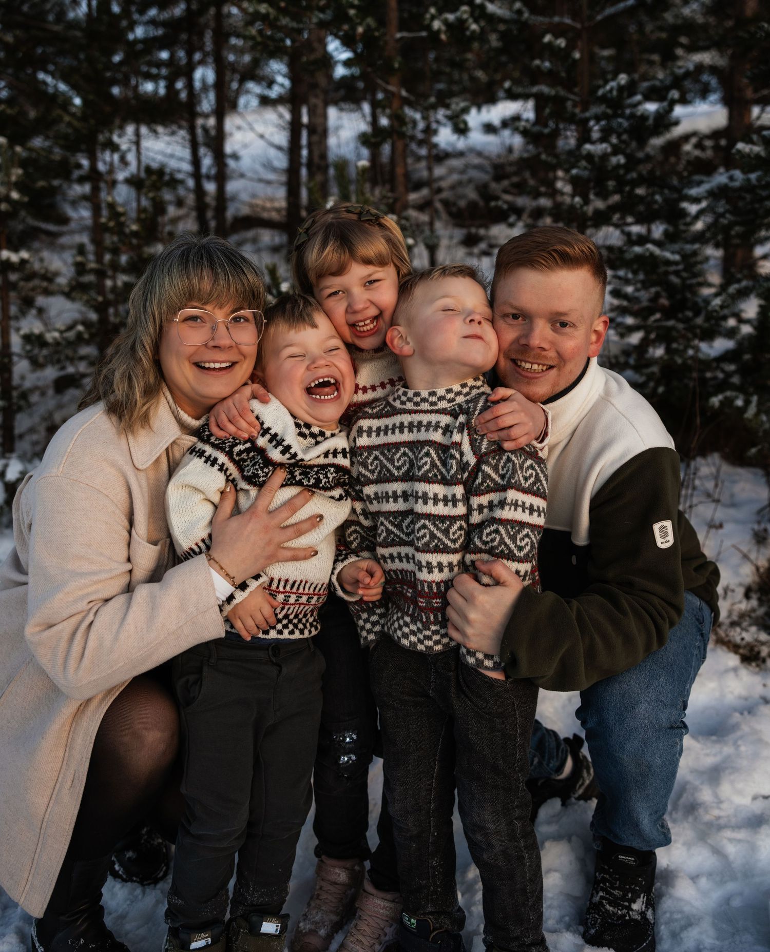Happy family of five posing together in a snowy winter forest, wearing matching Nordic sweaters.