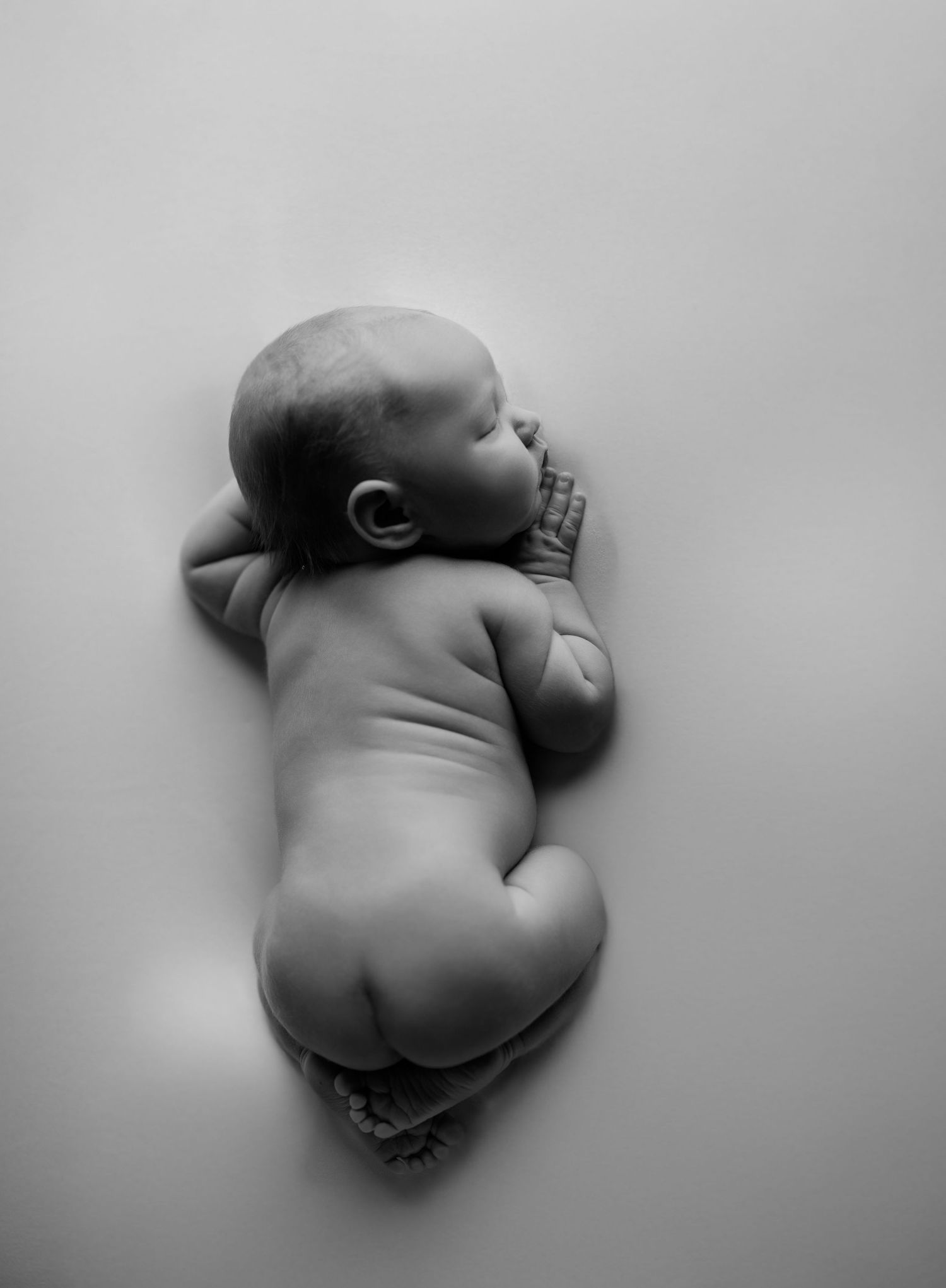 Black and white photo of a sleeping newborn baby lying on their side in a peaceful curled position.