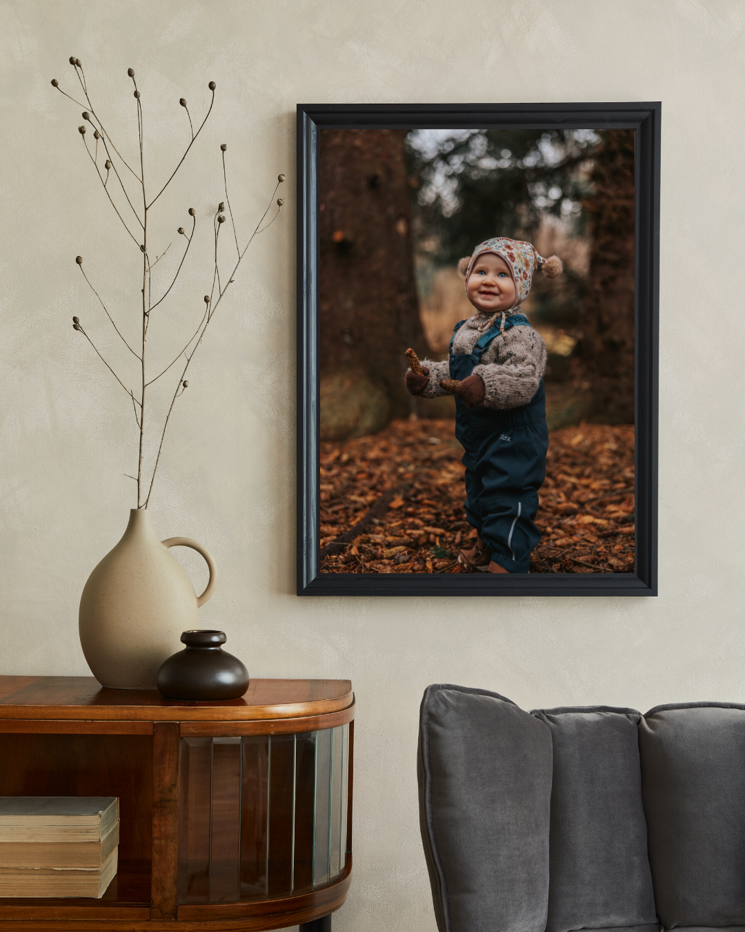 Framed photo of a smiling toddler in autumn leaves, displayed on a wall above a wooden console table with a vase.