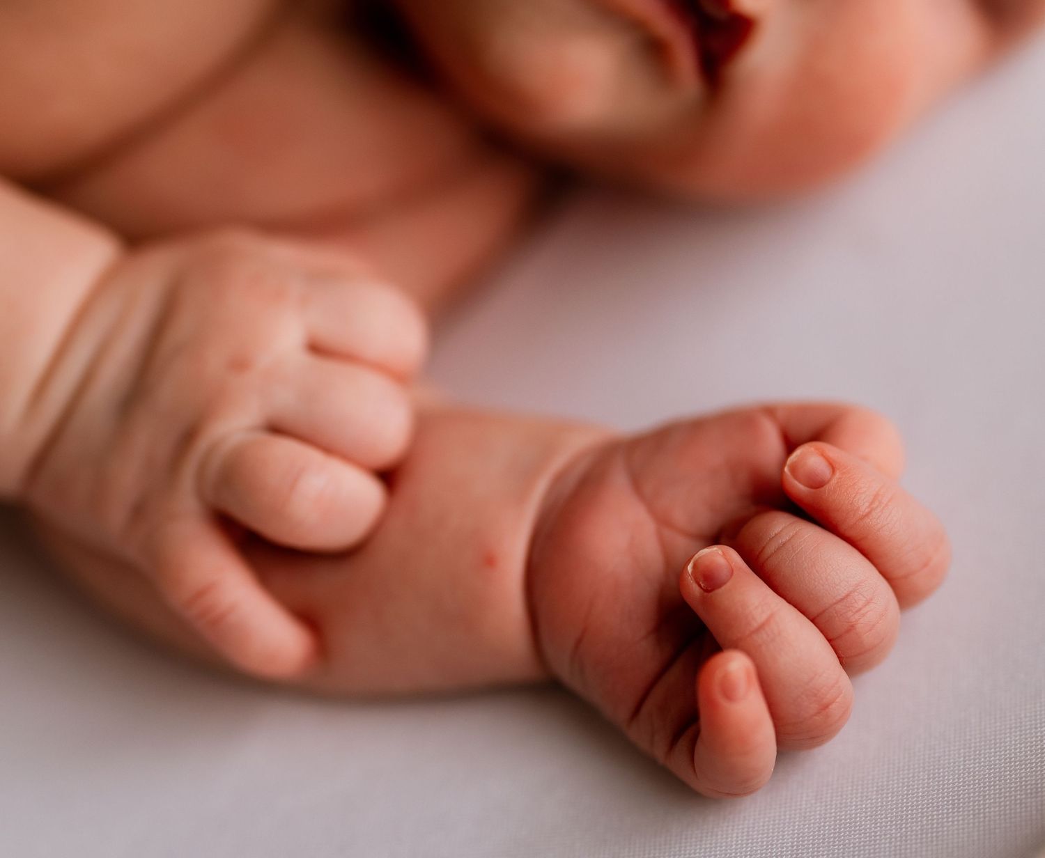 Close-up of a newborn baby's tiny hands and fingers resting on a soft white surface.