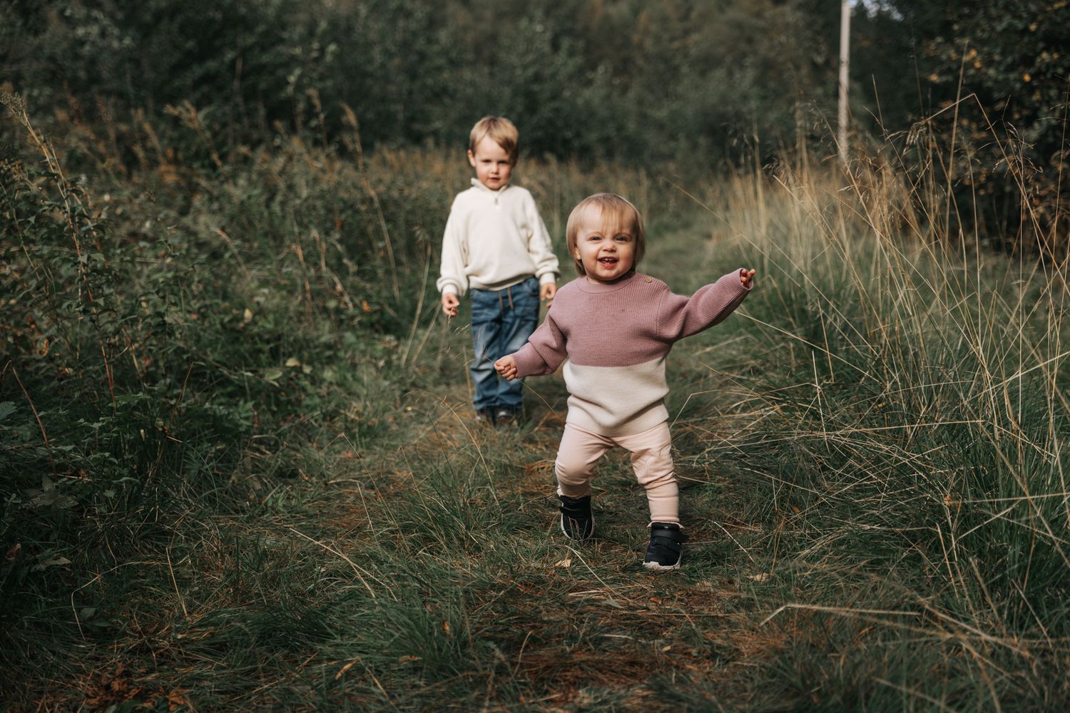 Two young children running and playing on a scenic grassy outdoor trail.