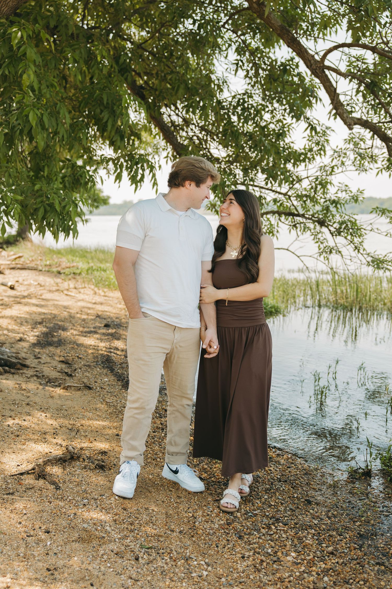 Couple holding hands and looking at each other lovingly near a reflective lakeside.