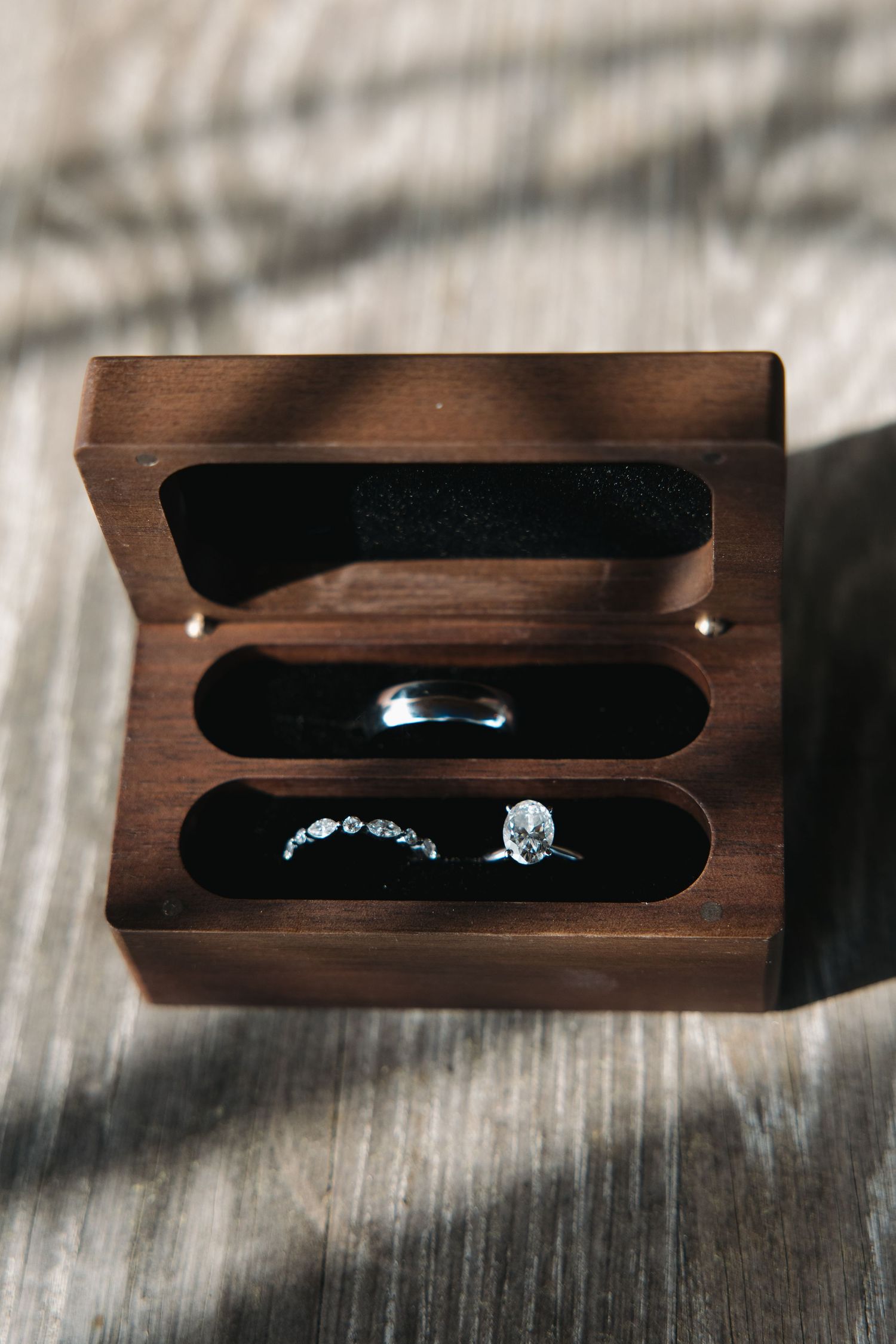 Wedding rings displayed in a wooden ring box with black velvet lining on a rustic wood surface.