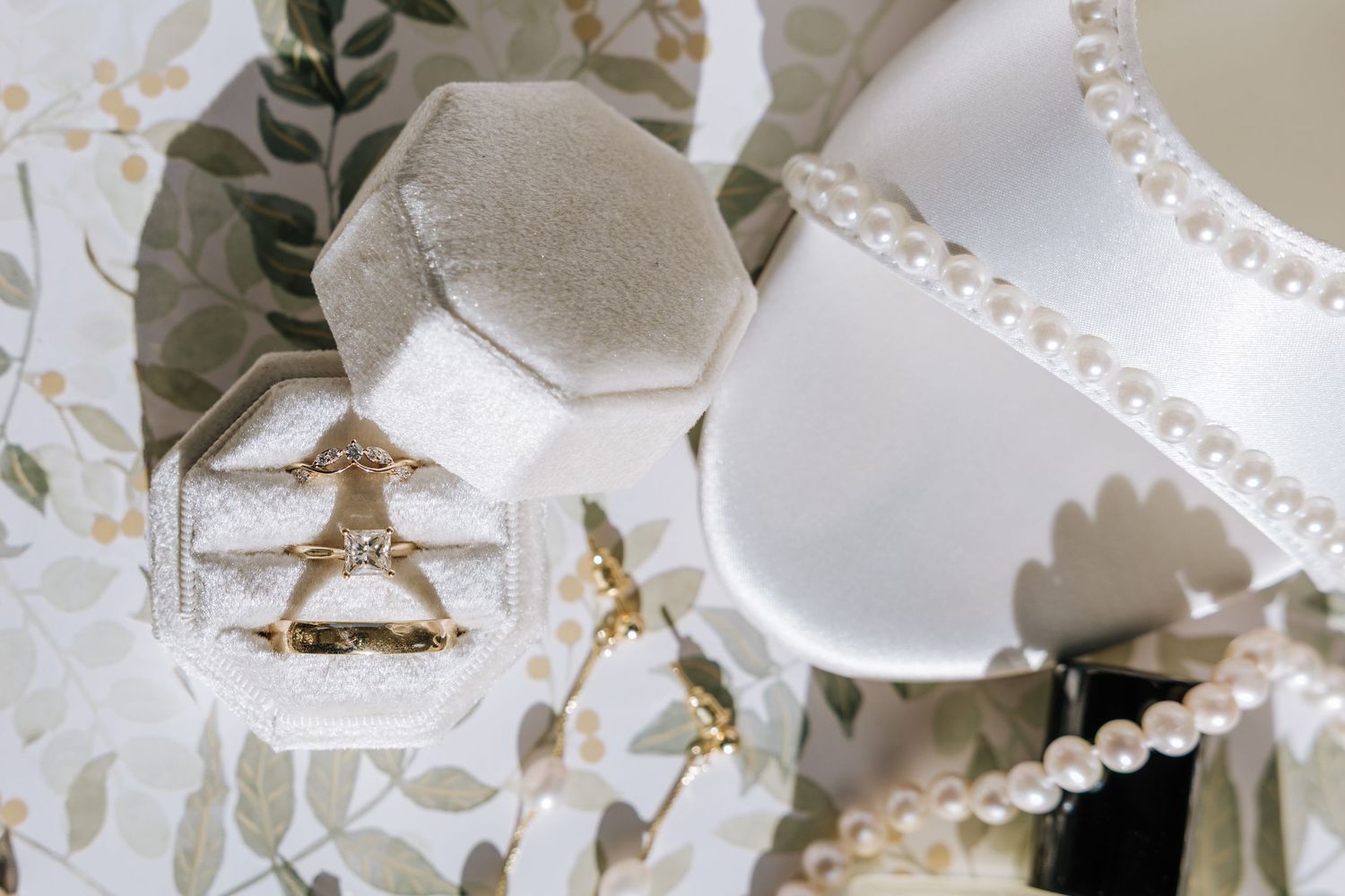 Elegant gold diamond ring in velvet hexagon box beside pearl necklace and white heels.