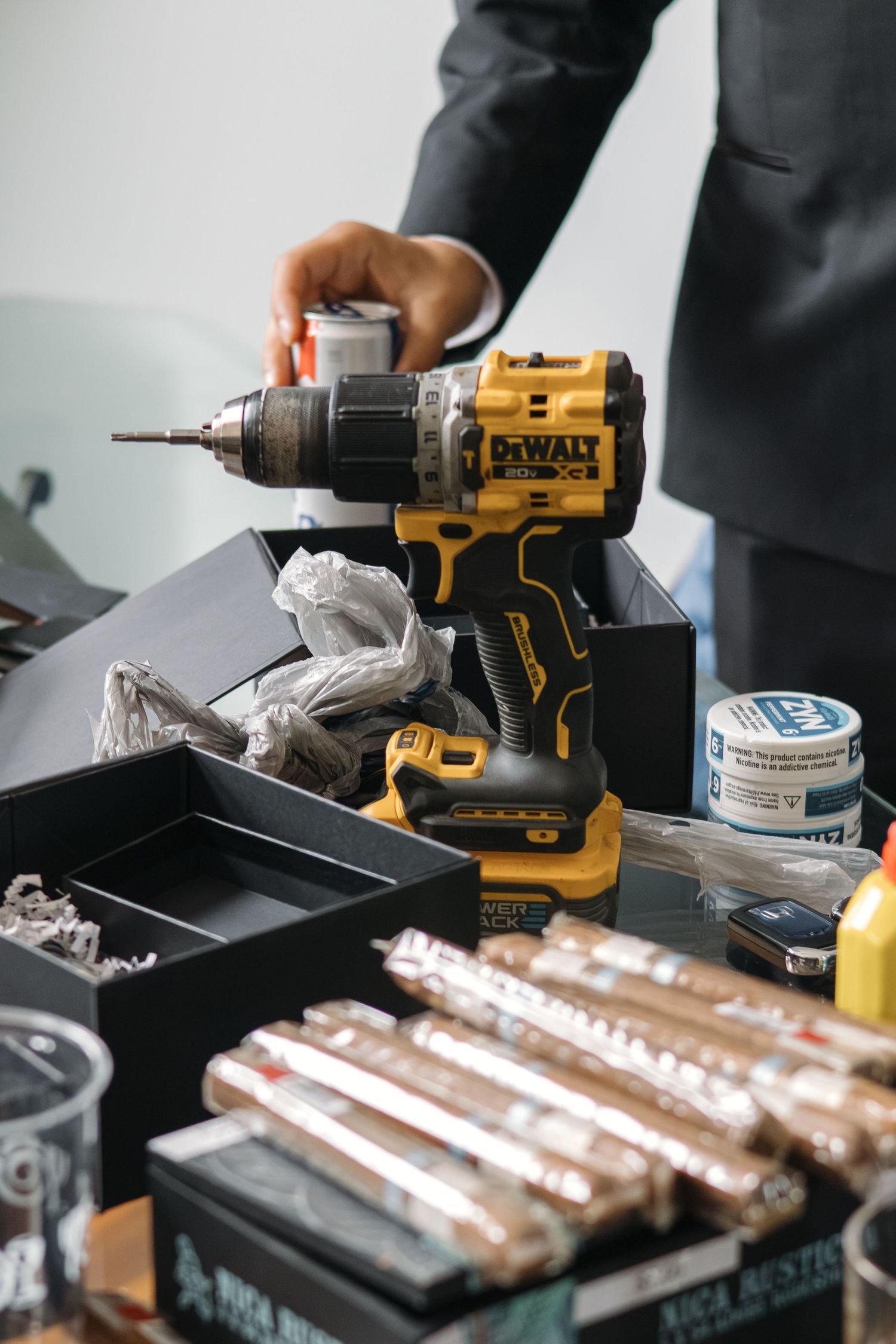 Groom holding DeWalt power drill over groomsmen gift box filled with cigars and tools.