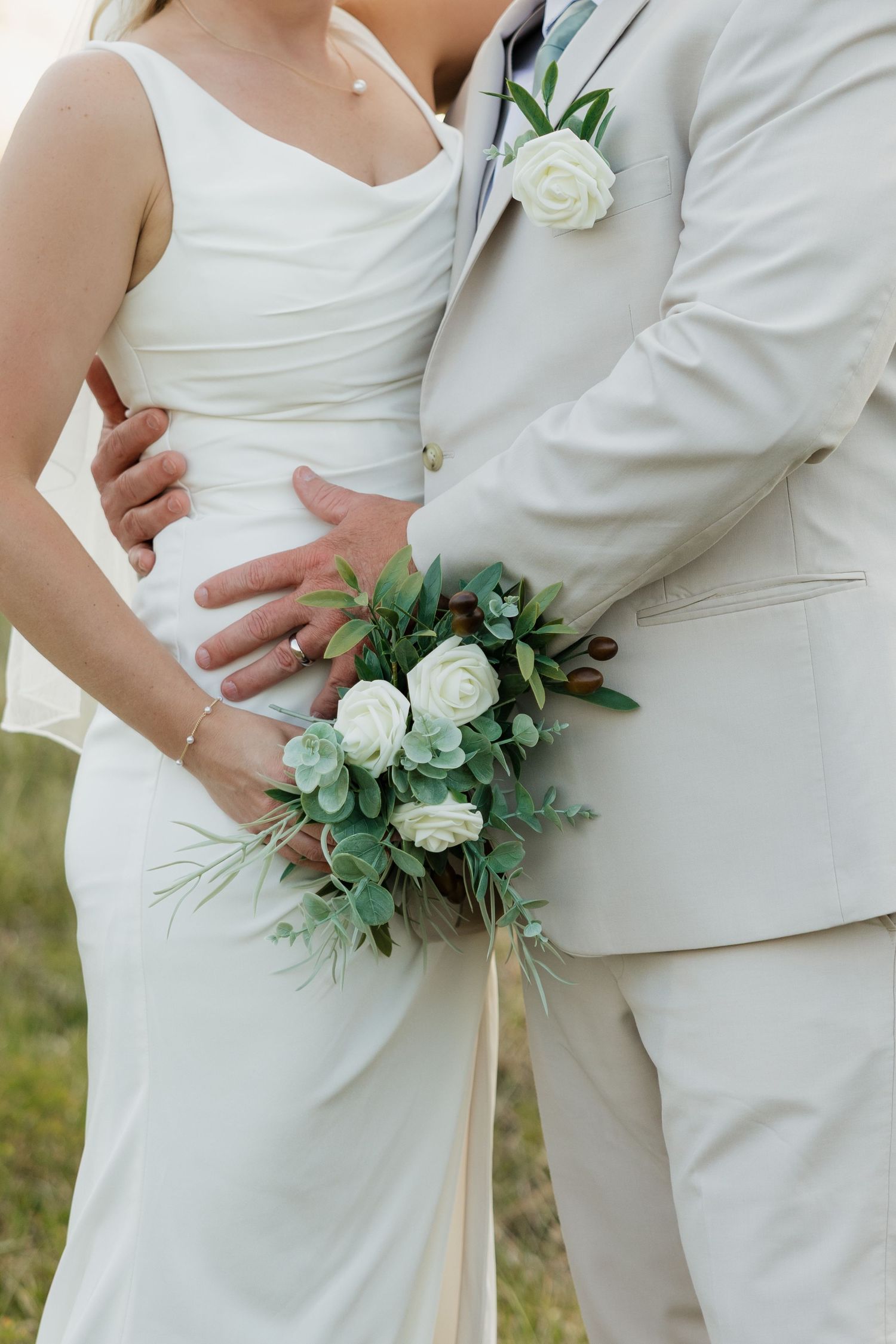 Close-up of bride and groom holding a white rose and greenery bouquet on their wedding day.