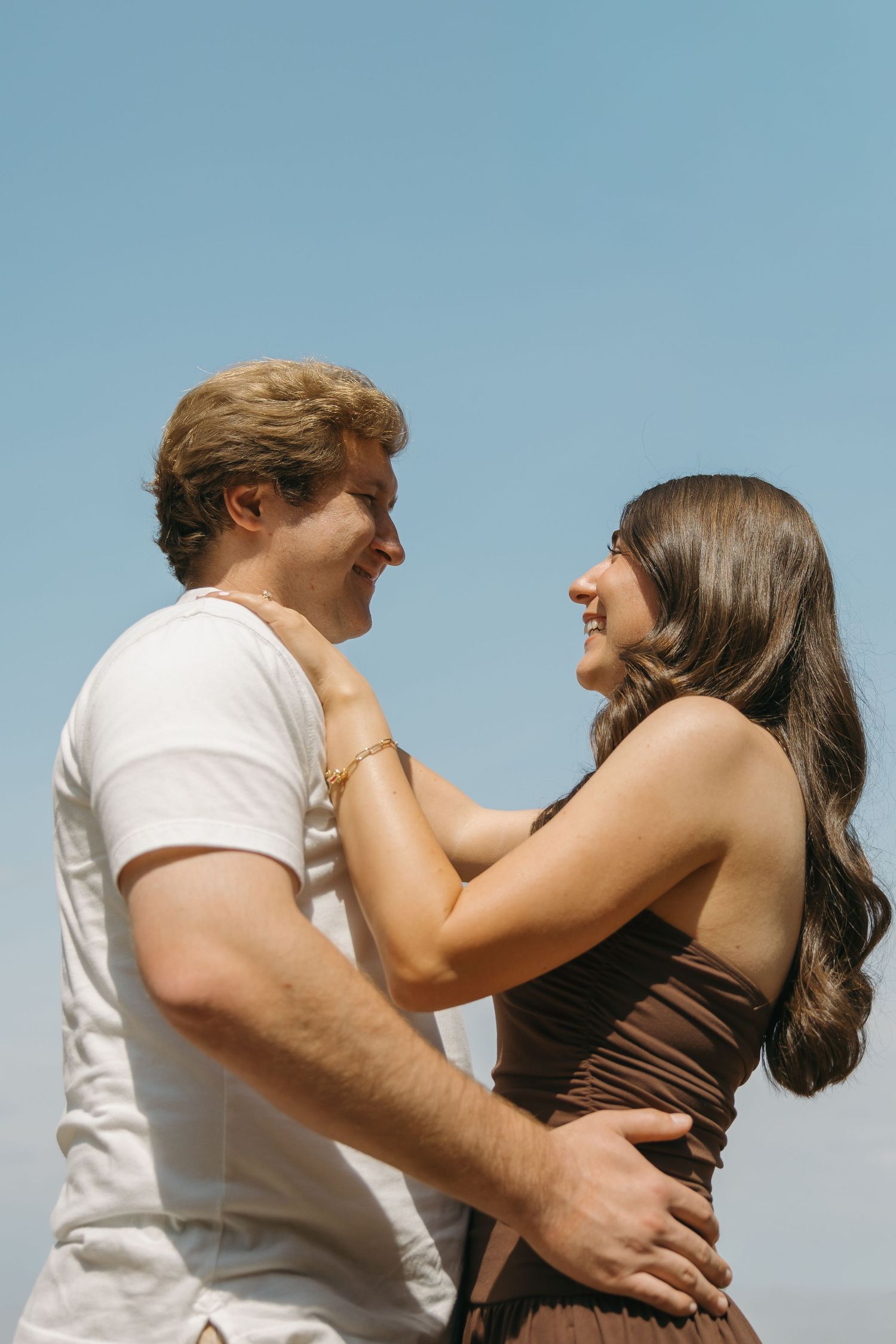 Happy couple hugging and laughing together outdoors under a clear sunny blue sky.