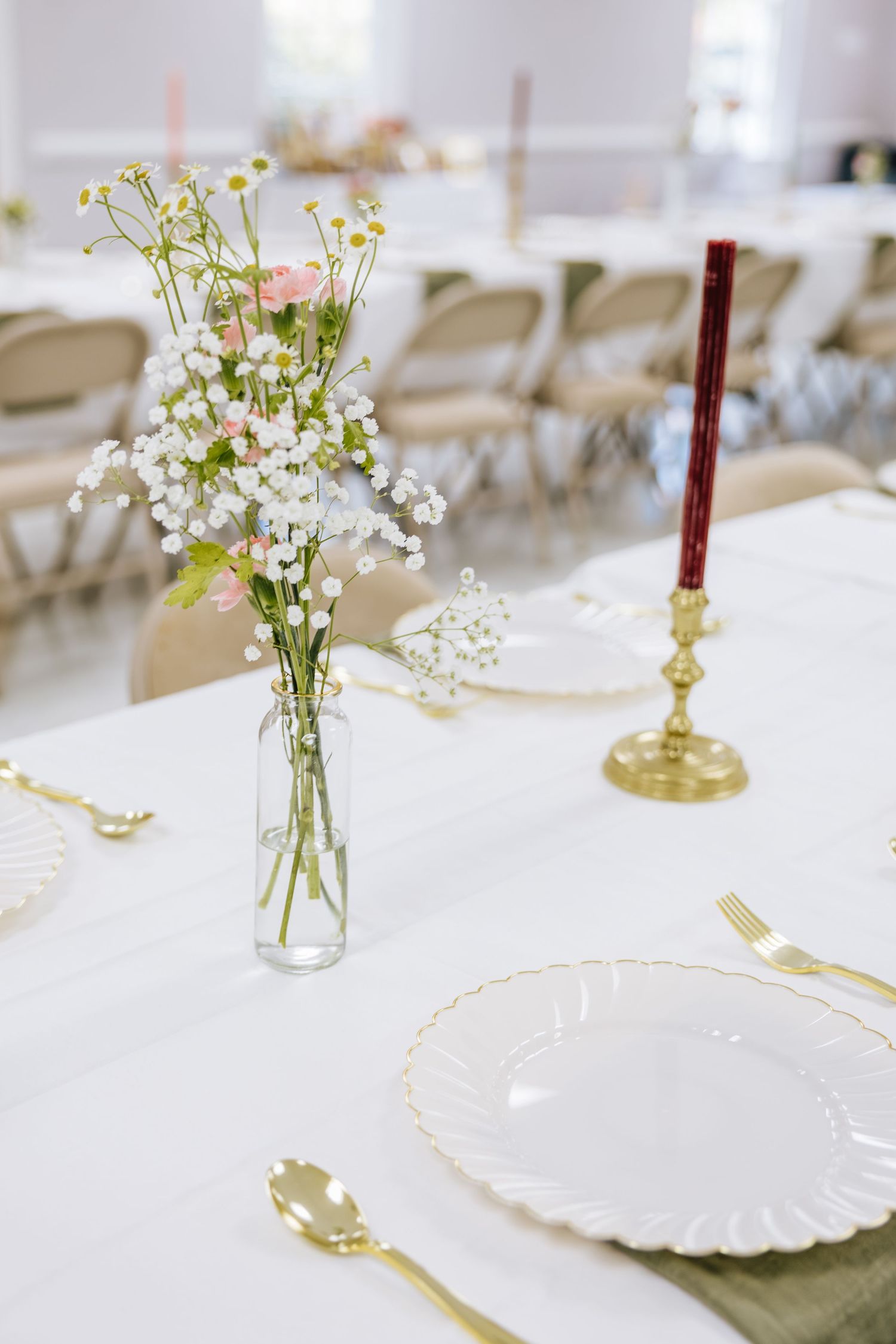 Wedding reception table with wildflower centerpiece, gold cutlery, and red taper candle.