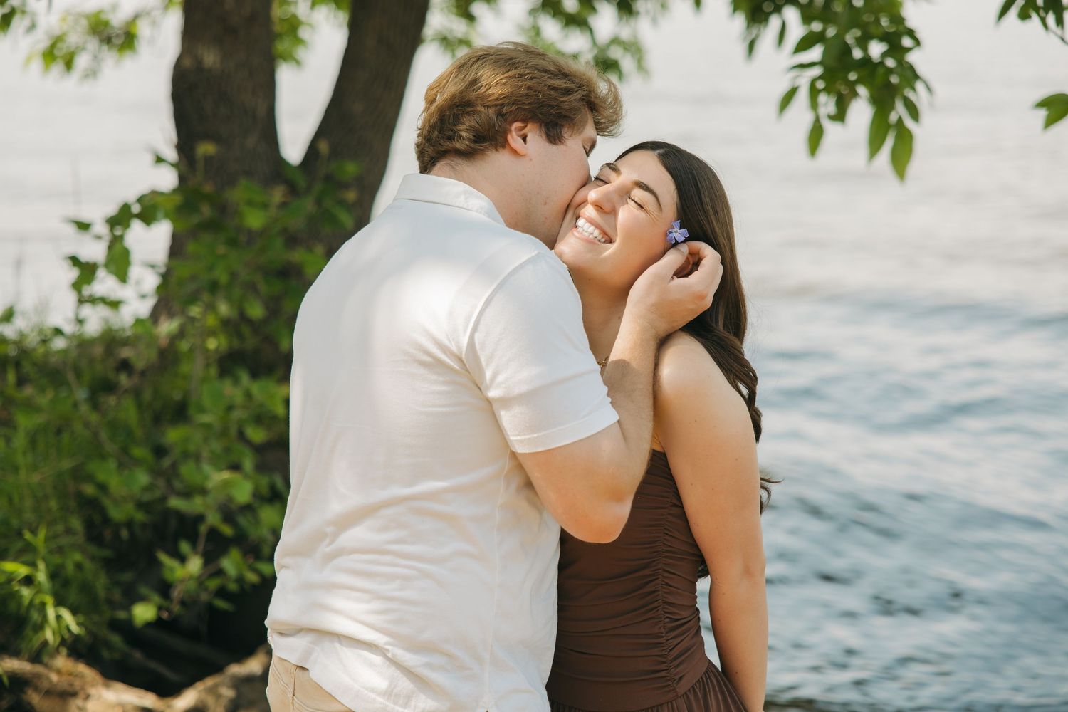 Happy couple laughing and embracing near a peaceful lakeside tree.