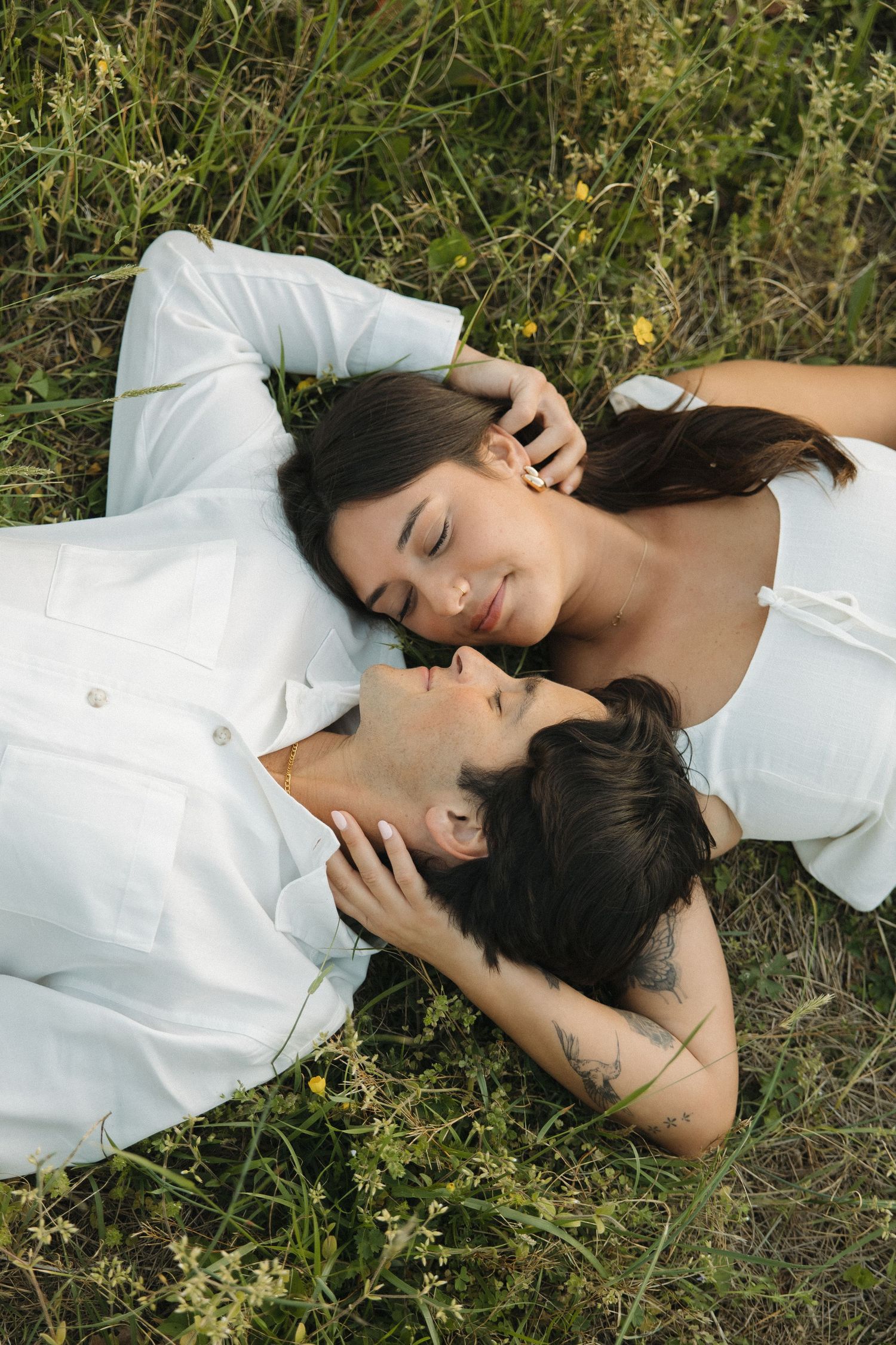 Couple lying in a wildflower meadow, facing each other tenderly in white outfits.