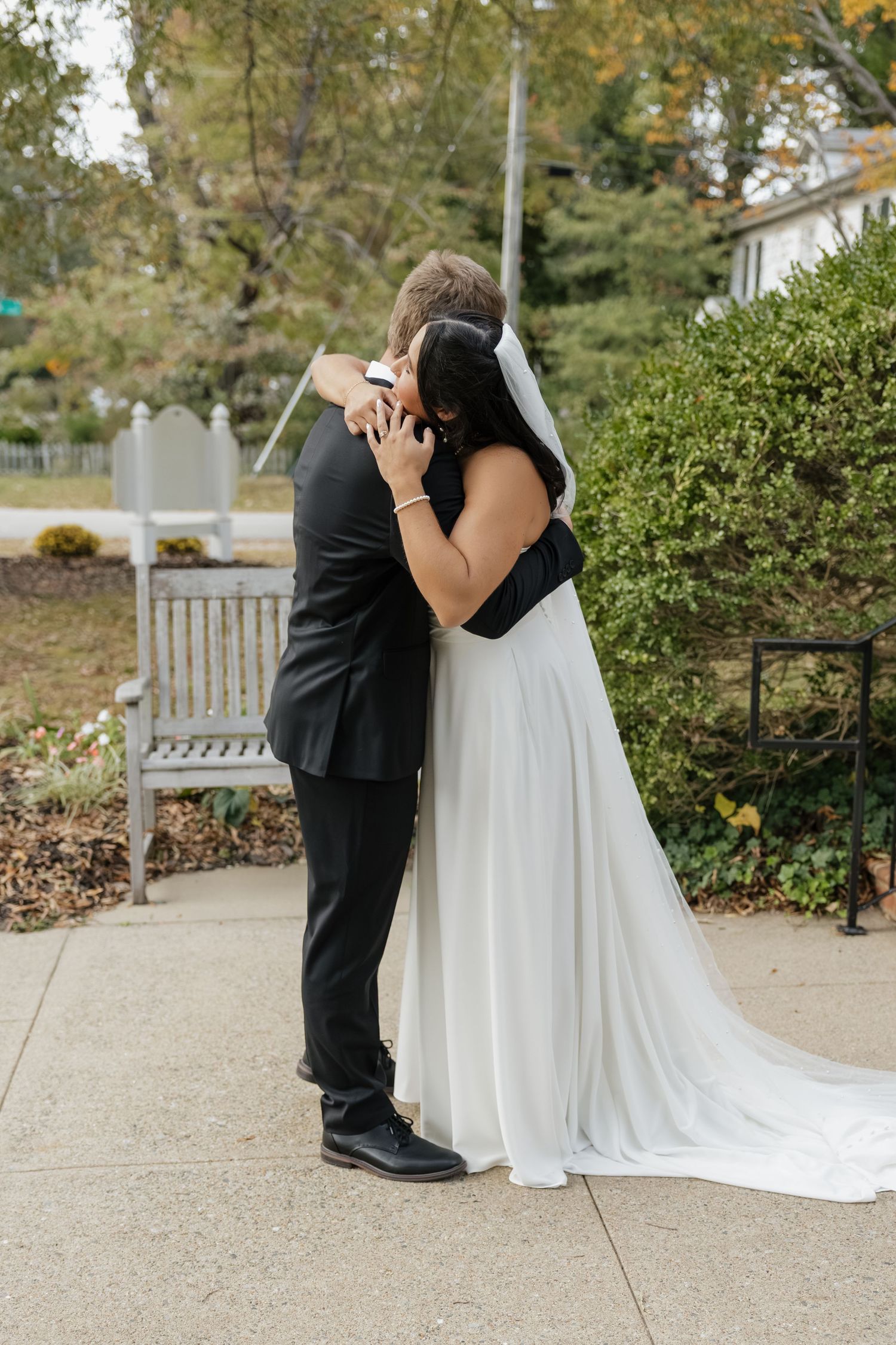 Bride and groom sharing a tender first kiss outdoors in a garden setting on their wedding day.