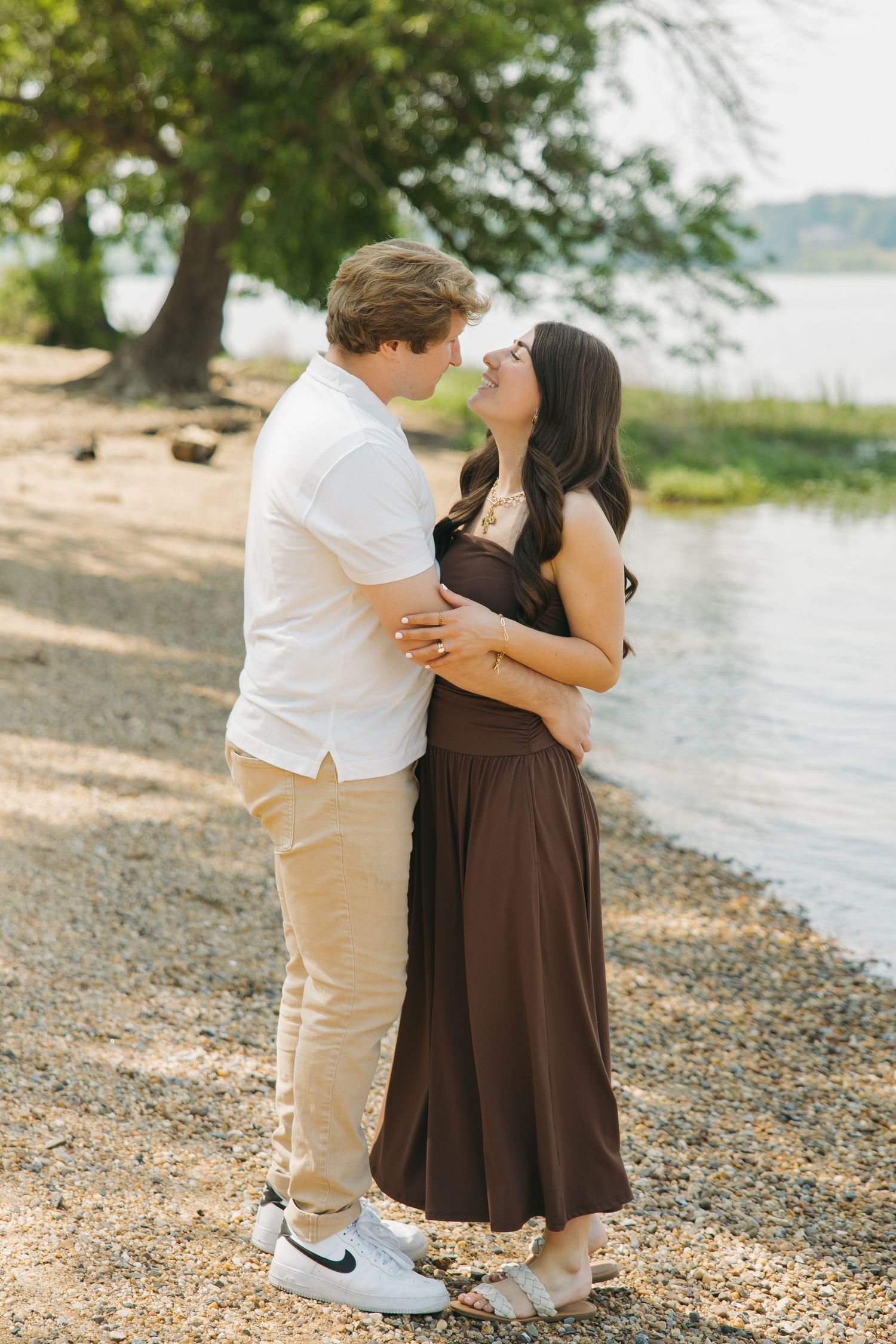 Couple holding each other close on a rocky shoreline near a lake.