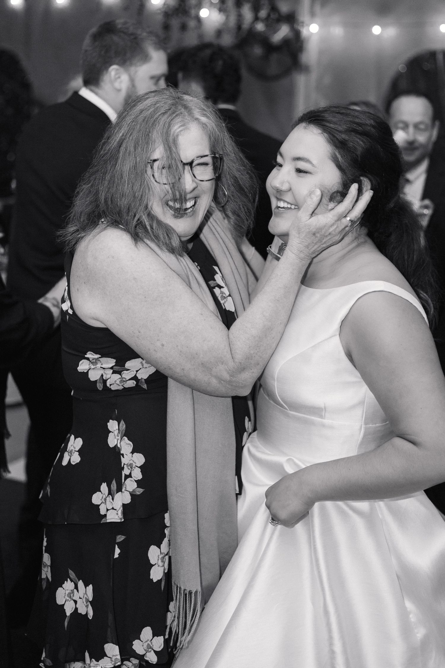 Black and white photo of older woman lovingly cupping bride's face during wedding reception dance.