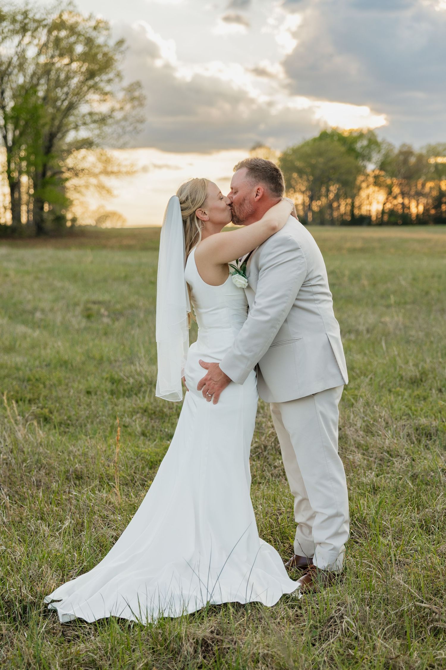 Bride and groom share a tender kiss in a golden field during their outdoor sunset wedding.