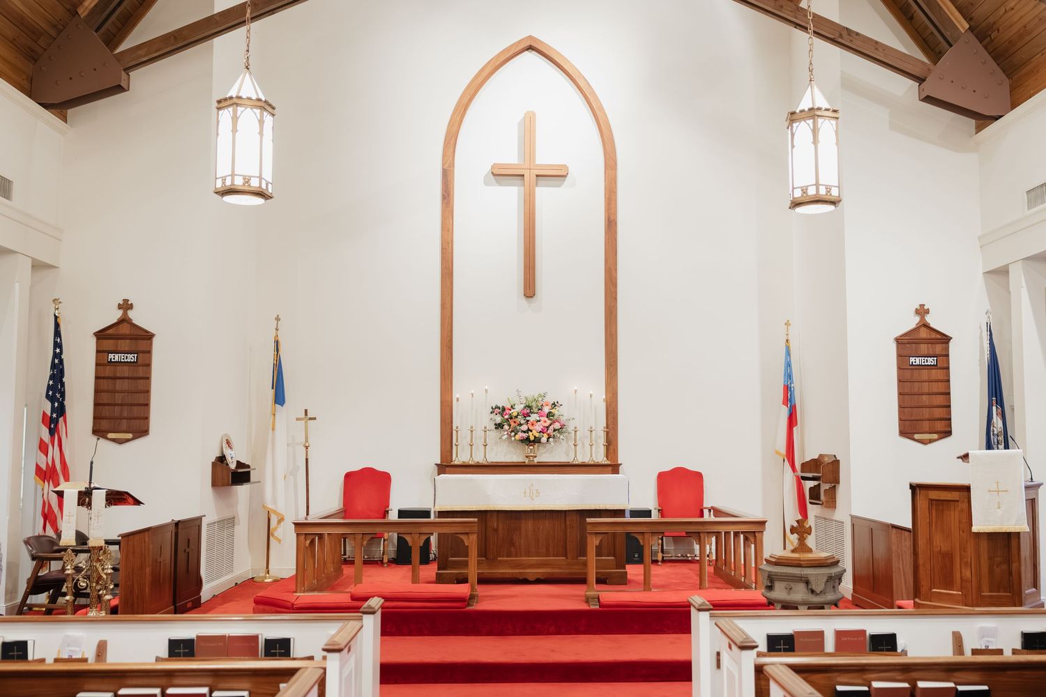 Classic white church interior with wooden cross, red carpet, and gold altar details.
