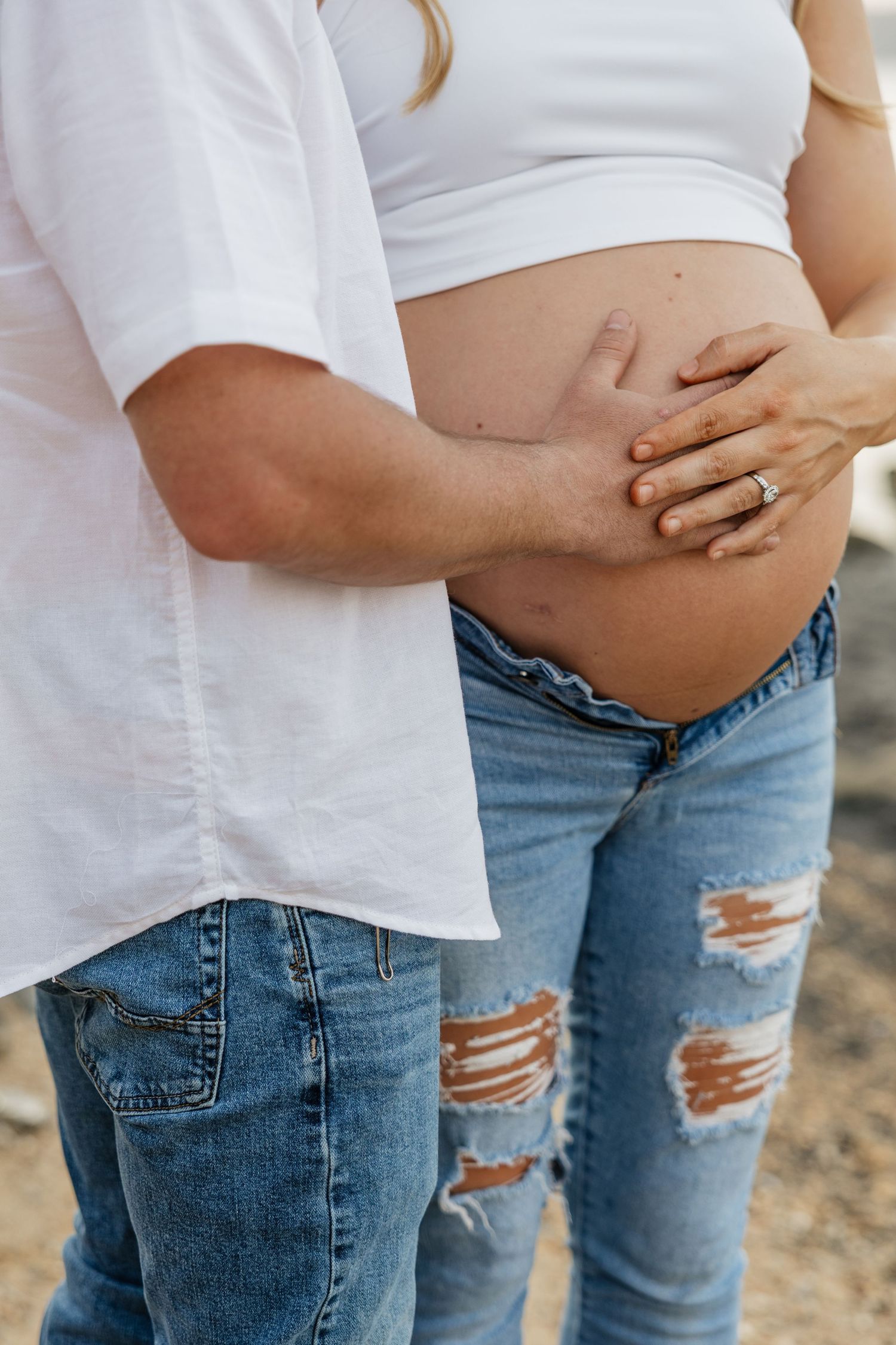 Close-up of couple's hands gently cradling pregnant baby bump, woman wearing wedding ring.