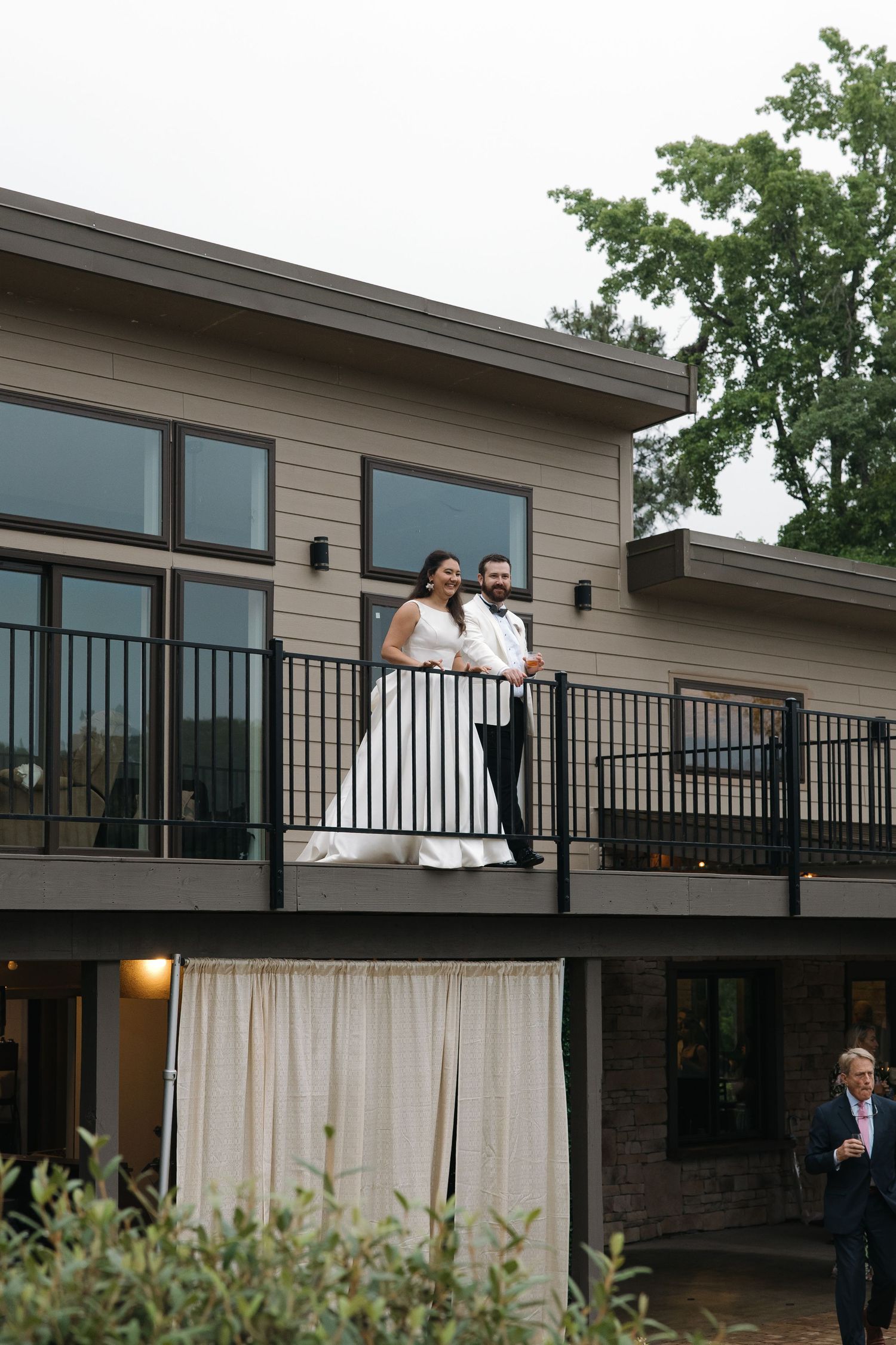 Bride and groom standing on a modern venue balcony smiling together on their wedding day.