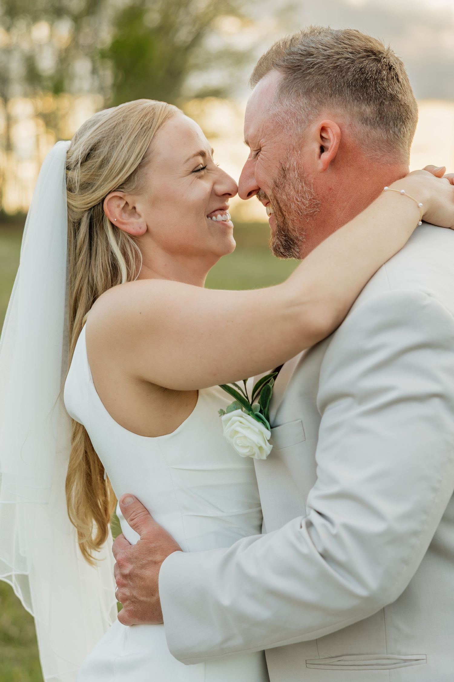 Close-up of a smiling bride and groom touching noses during their outdoor golden hour wedding.