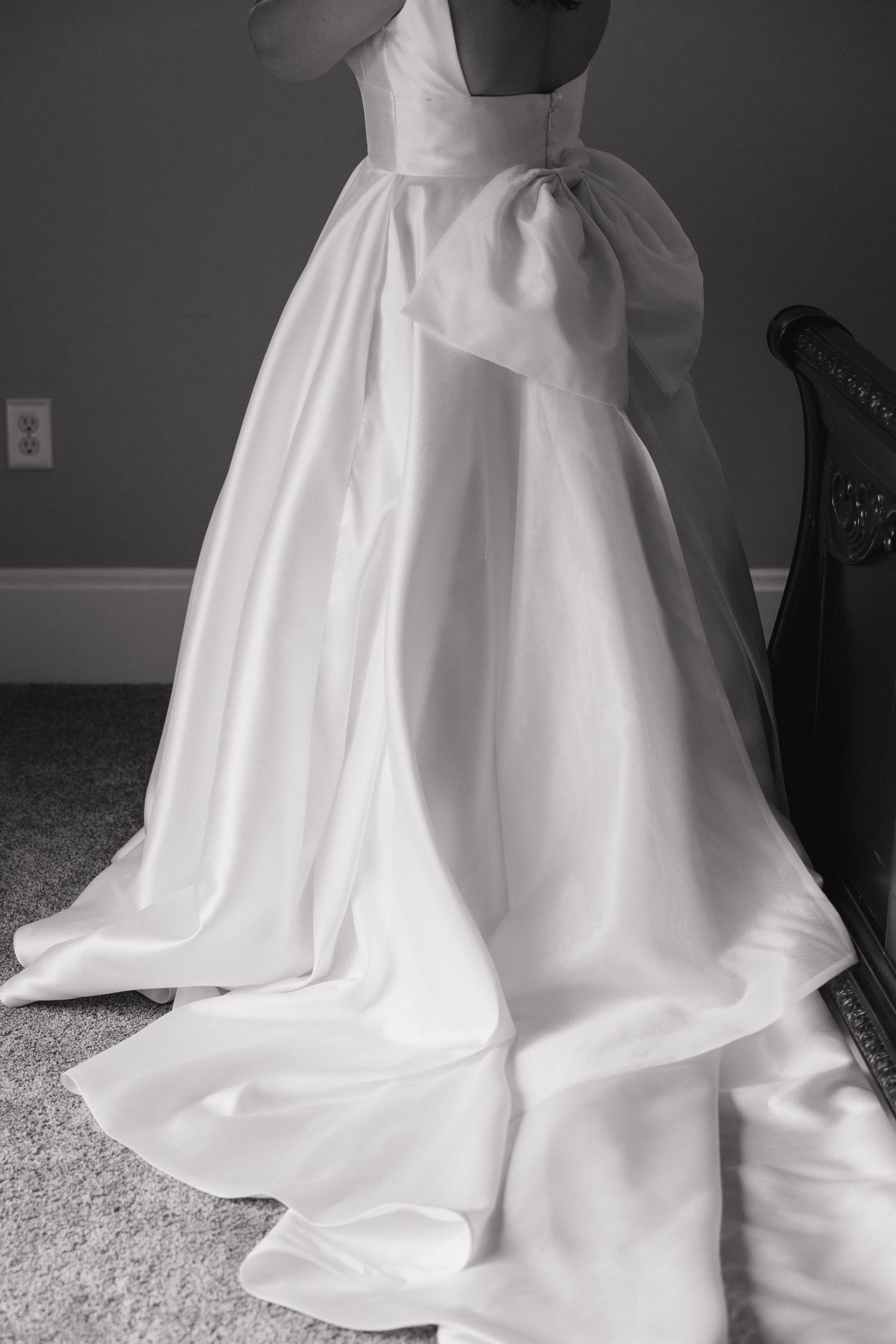 Close-up black and white photo of a satin wedding ball gown with elegant bow detail and flowing train.