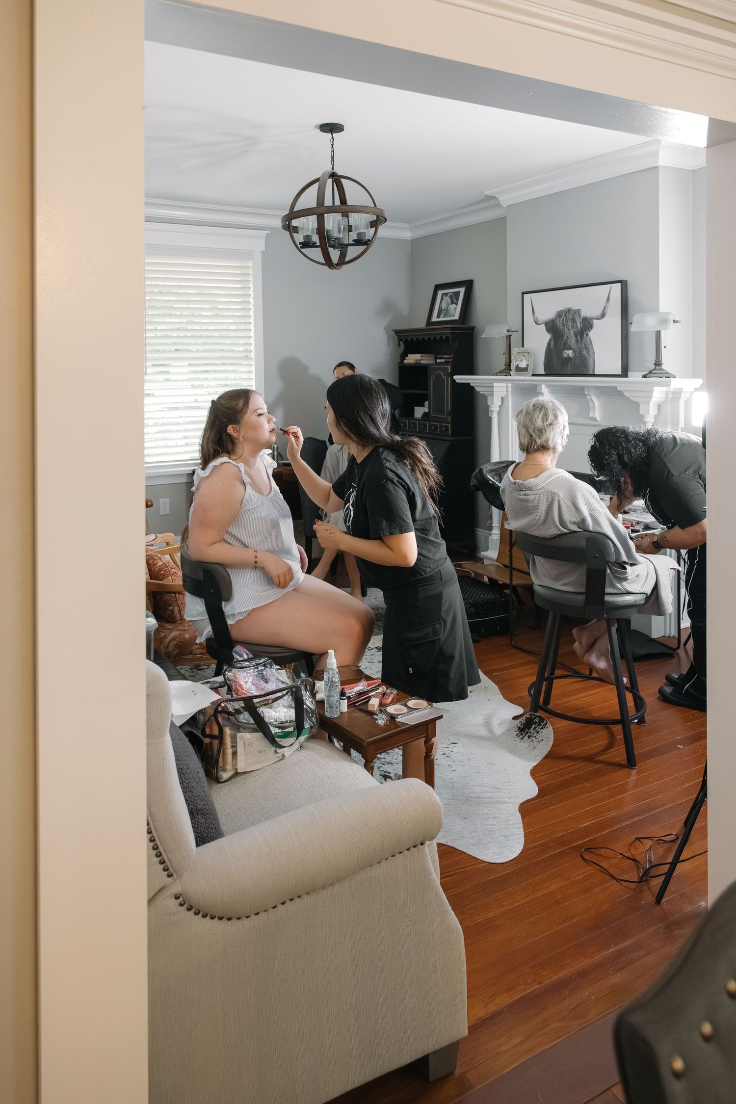 Bridesmaids getting hair and makeup done in elegant living room on wedding morning preparations.
