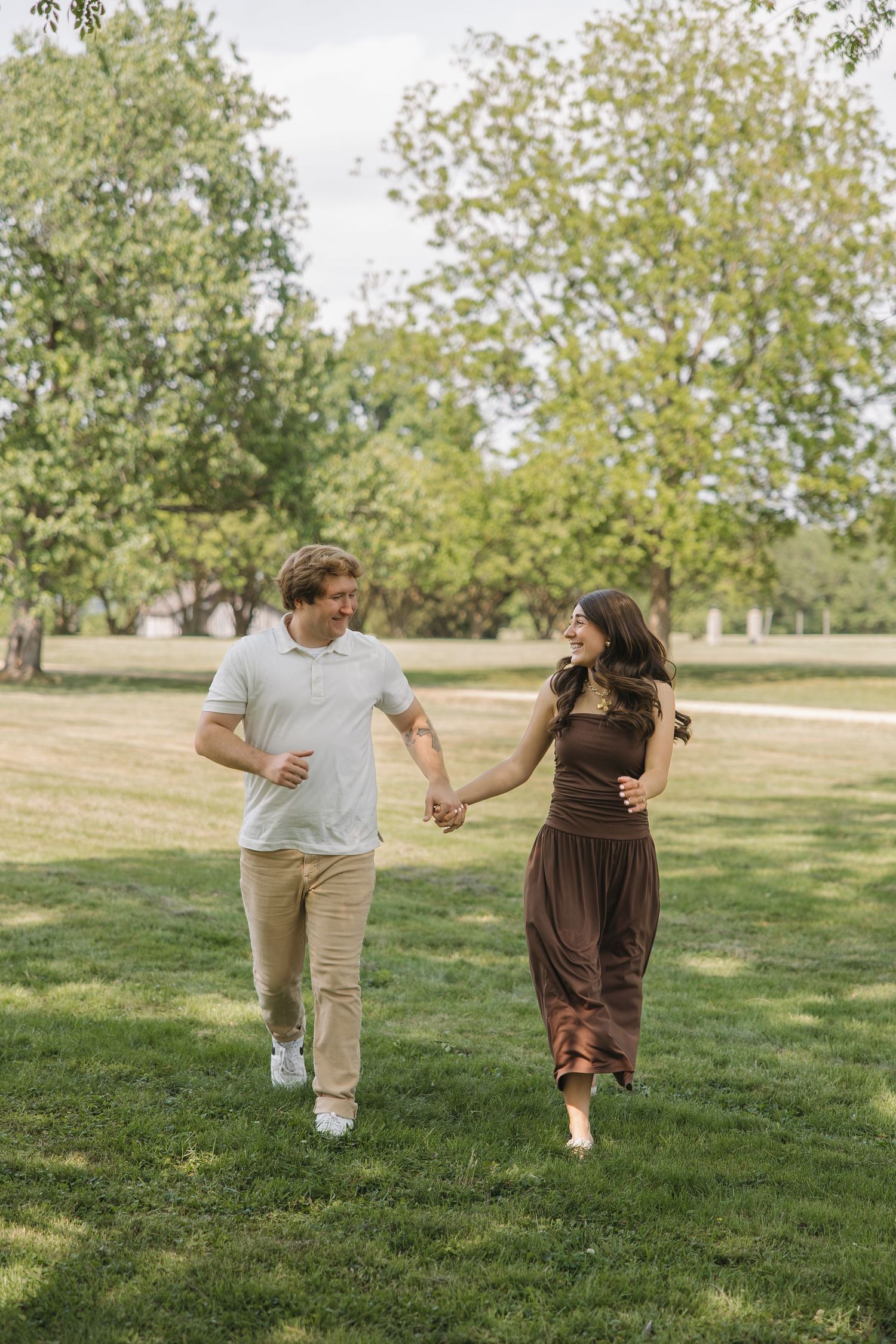 Happy couple holding hands and walking through a lush green park on a sunny day.