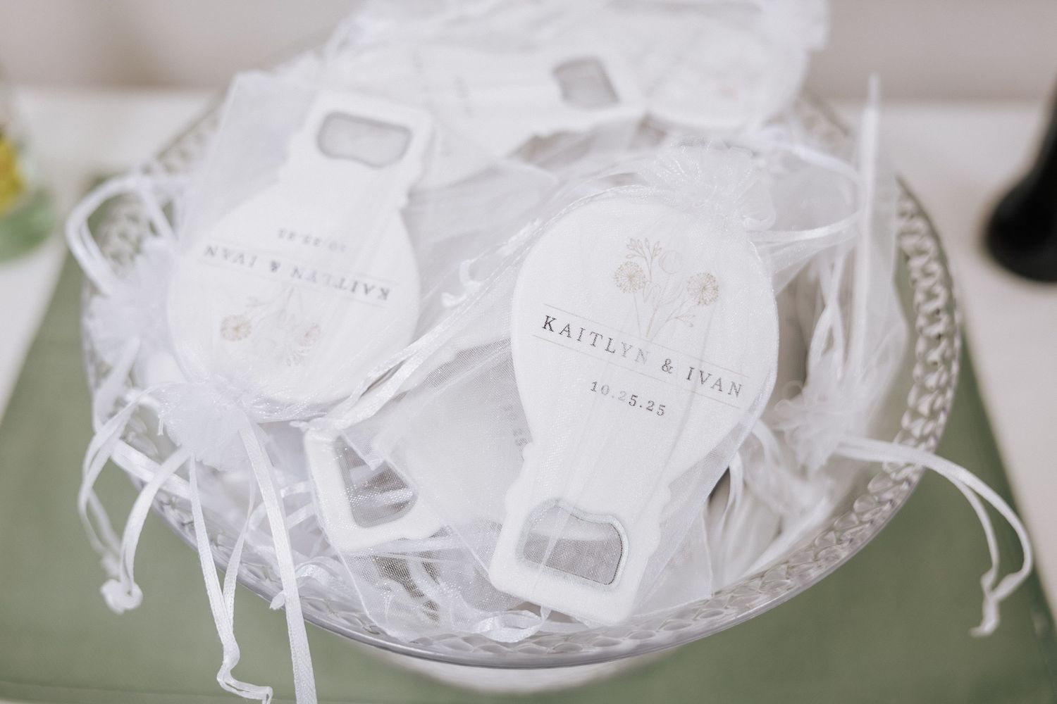 Personalized white bottle opener wedding favors wrapped in organza bags in decorative basket.
