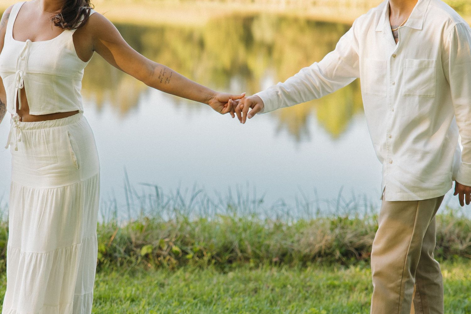 Couple holding hands near a serene reflective lake in a lush outdoor setting.