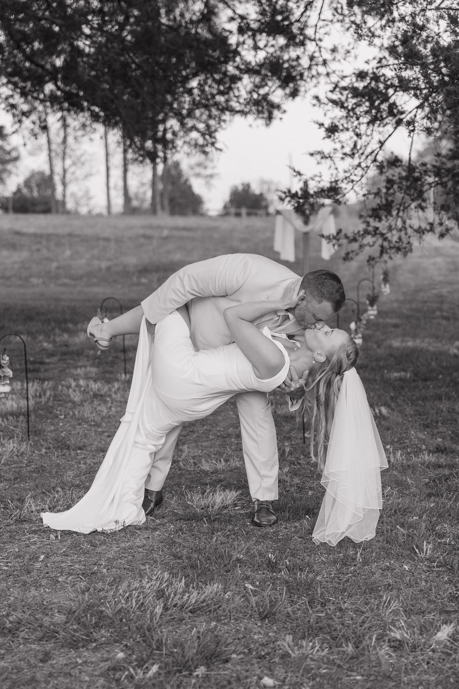 Groom dips bride for a romantic kiss in a black and white outdoor wedding photo.