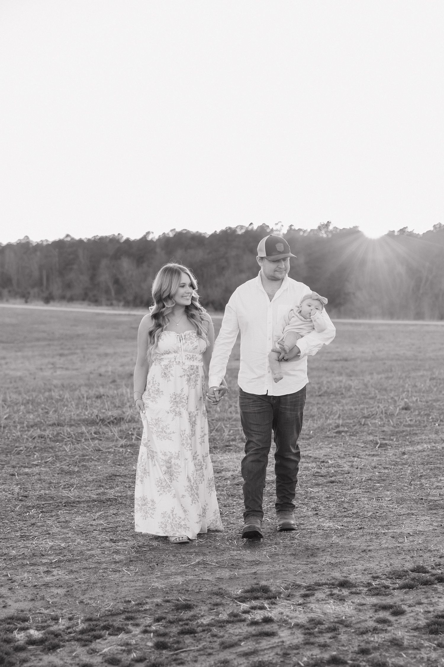 Black and white photo of young family walking through open field holding hands at sunset.