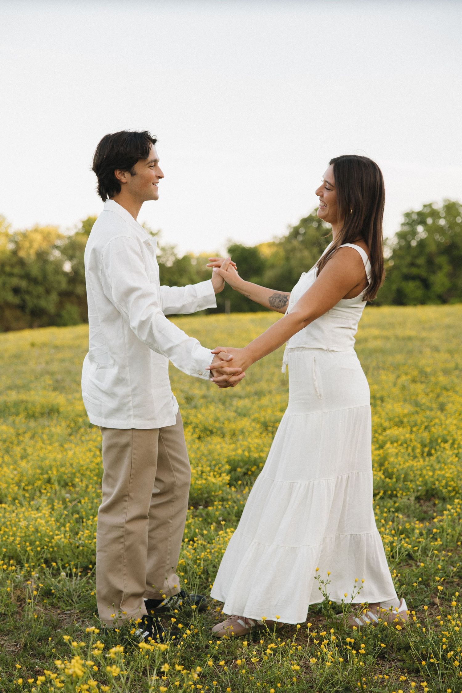 A joyful couple dances together holding hands in a sunny field of yellow wildflowers.