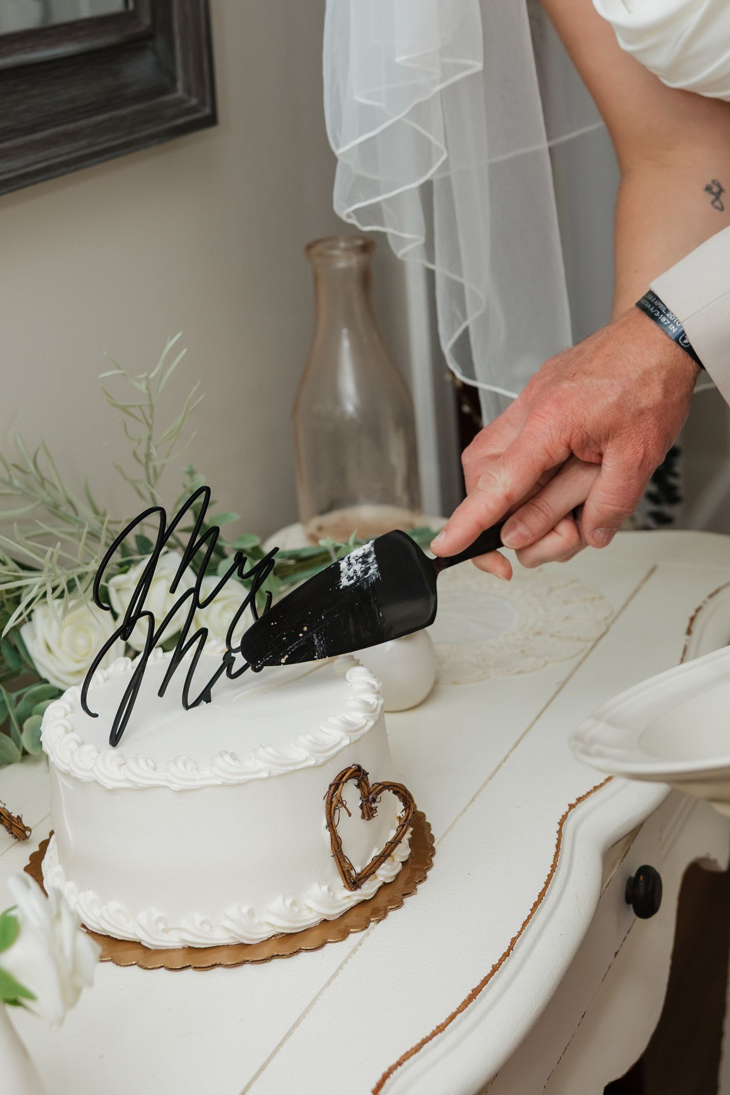 Close-up of groom cutting white wedding cake with Mr. and Mrs. calligraphy design using black server.