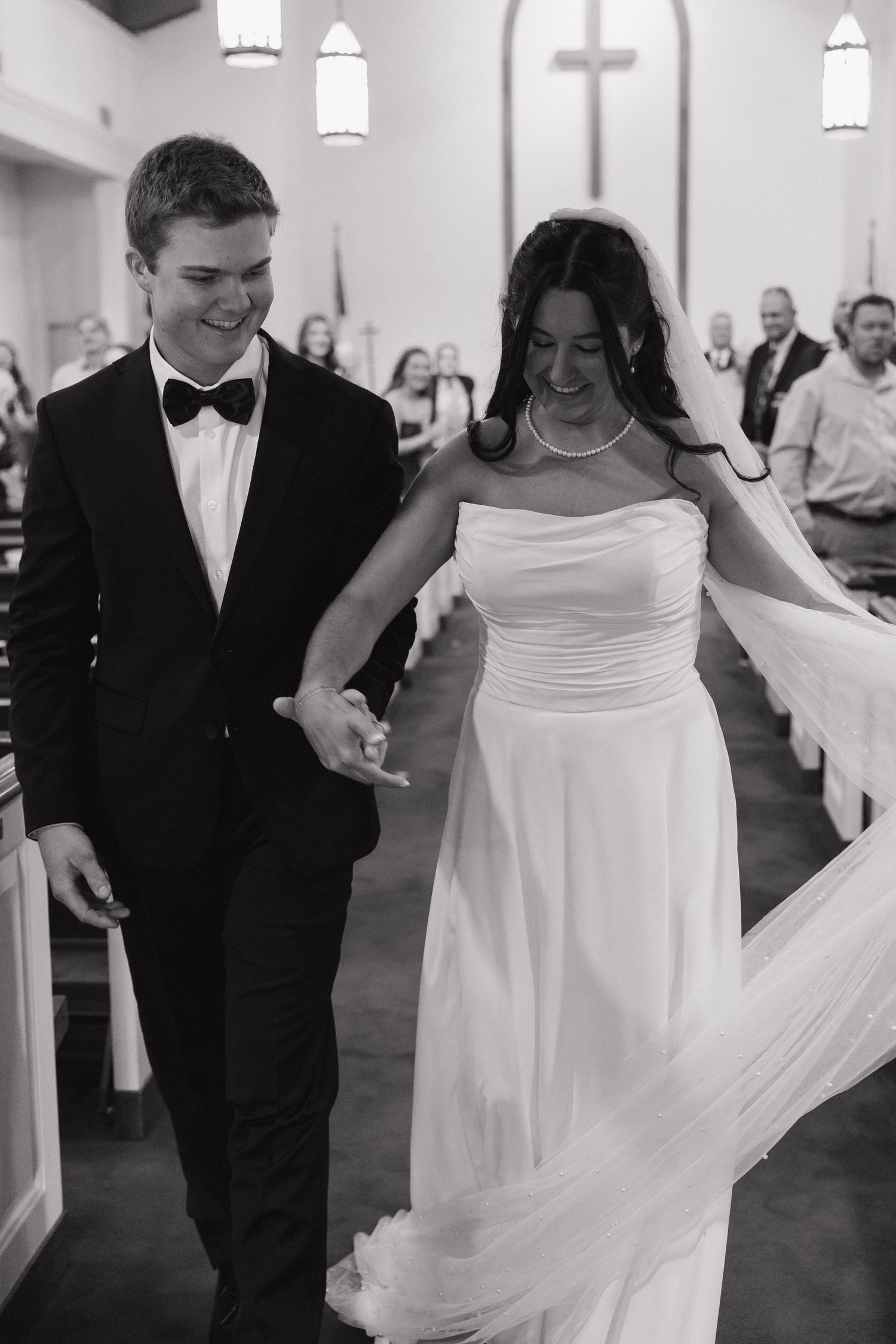 Black and white photo of smiling bride and groom walking down church aisle after wedding ceremony.