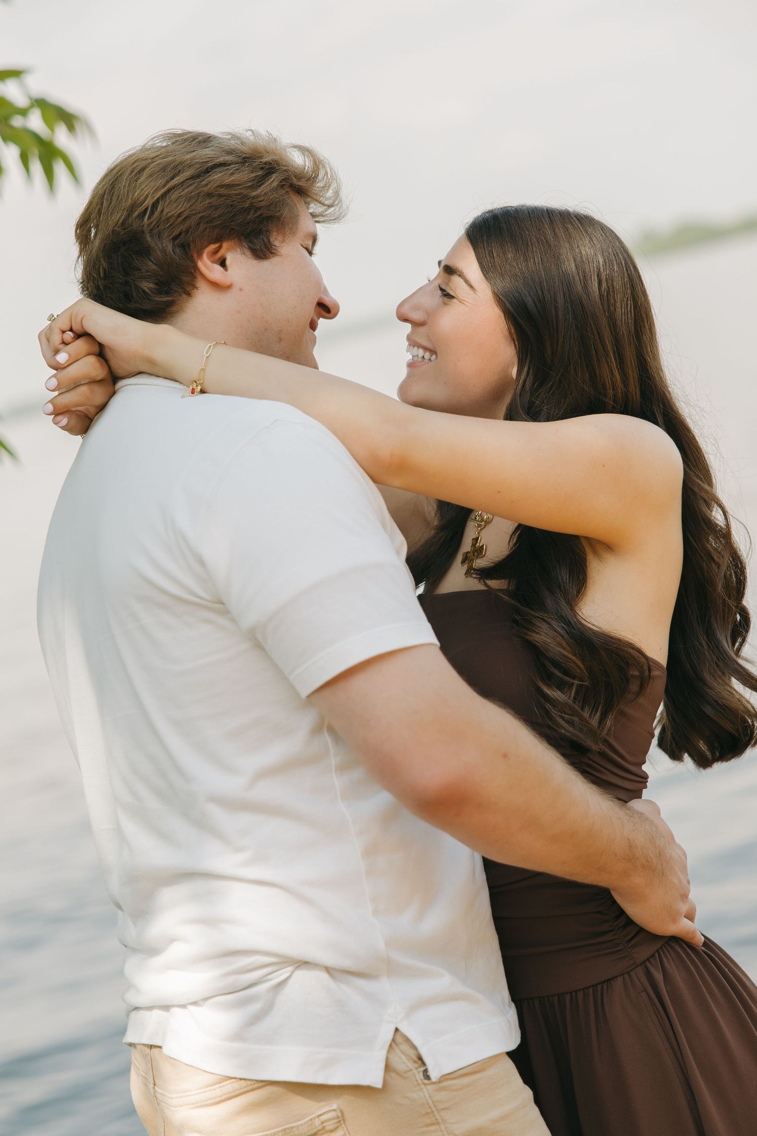 Smiling couple embracing and gazing at each other near a calm lake.