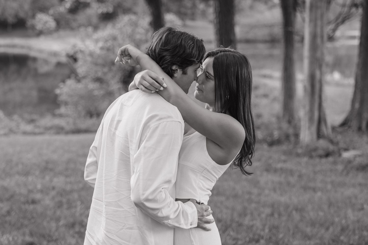 Black and white photo of a couple embracing closely outdoors in a park setting.