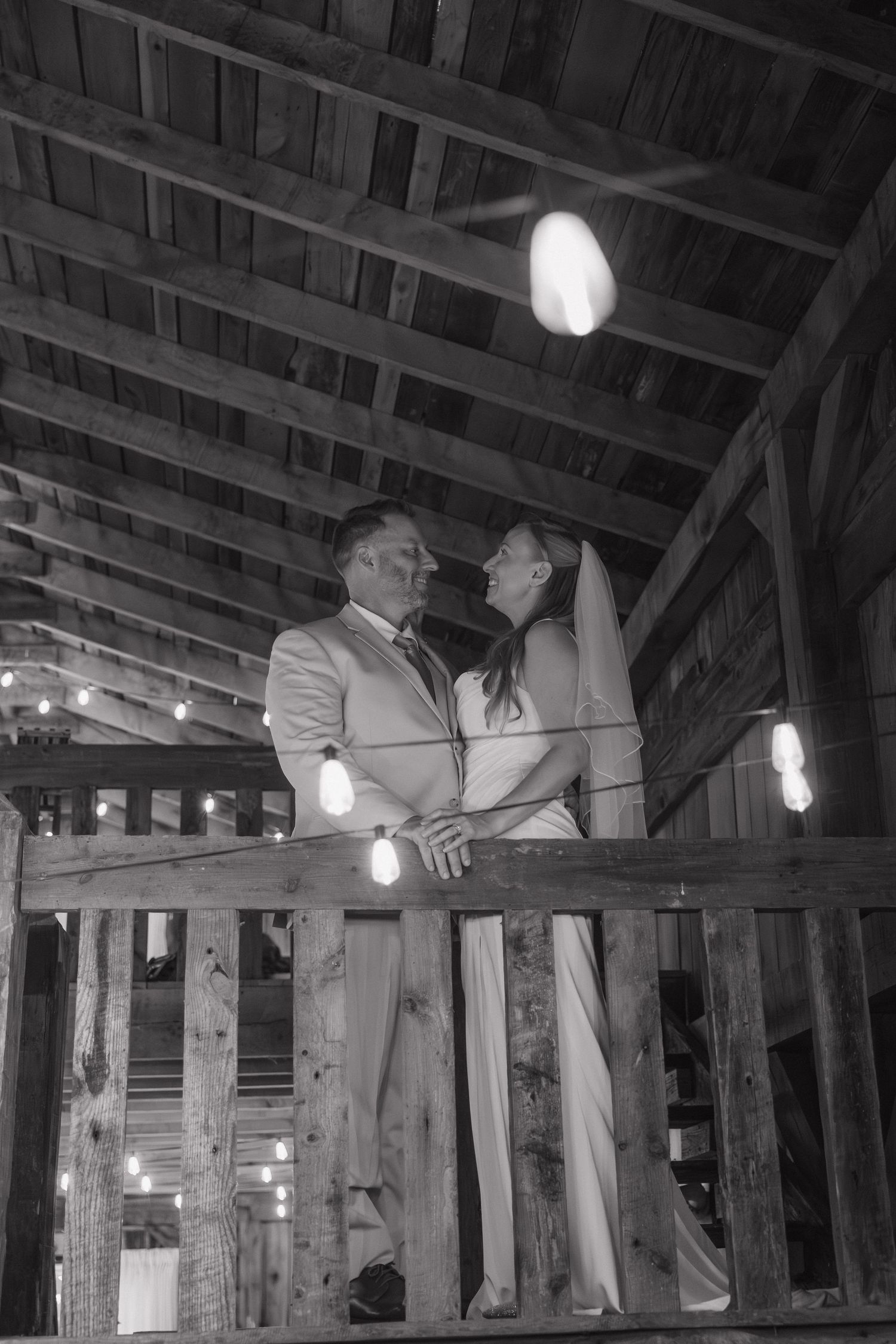 Bride and groom sharing an intimate moment on a wooden balcony inside a rustic barn venue.