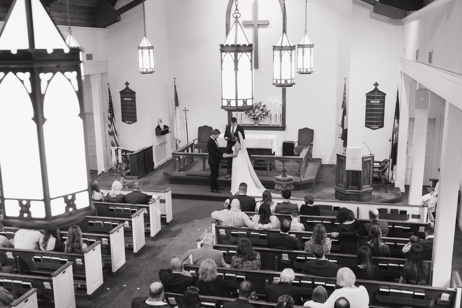 Black and white aerial view of intimate wedding ceremony inside a traditional church with wooden pews.