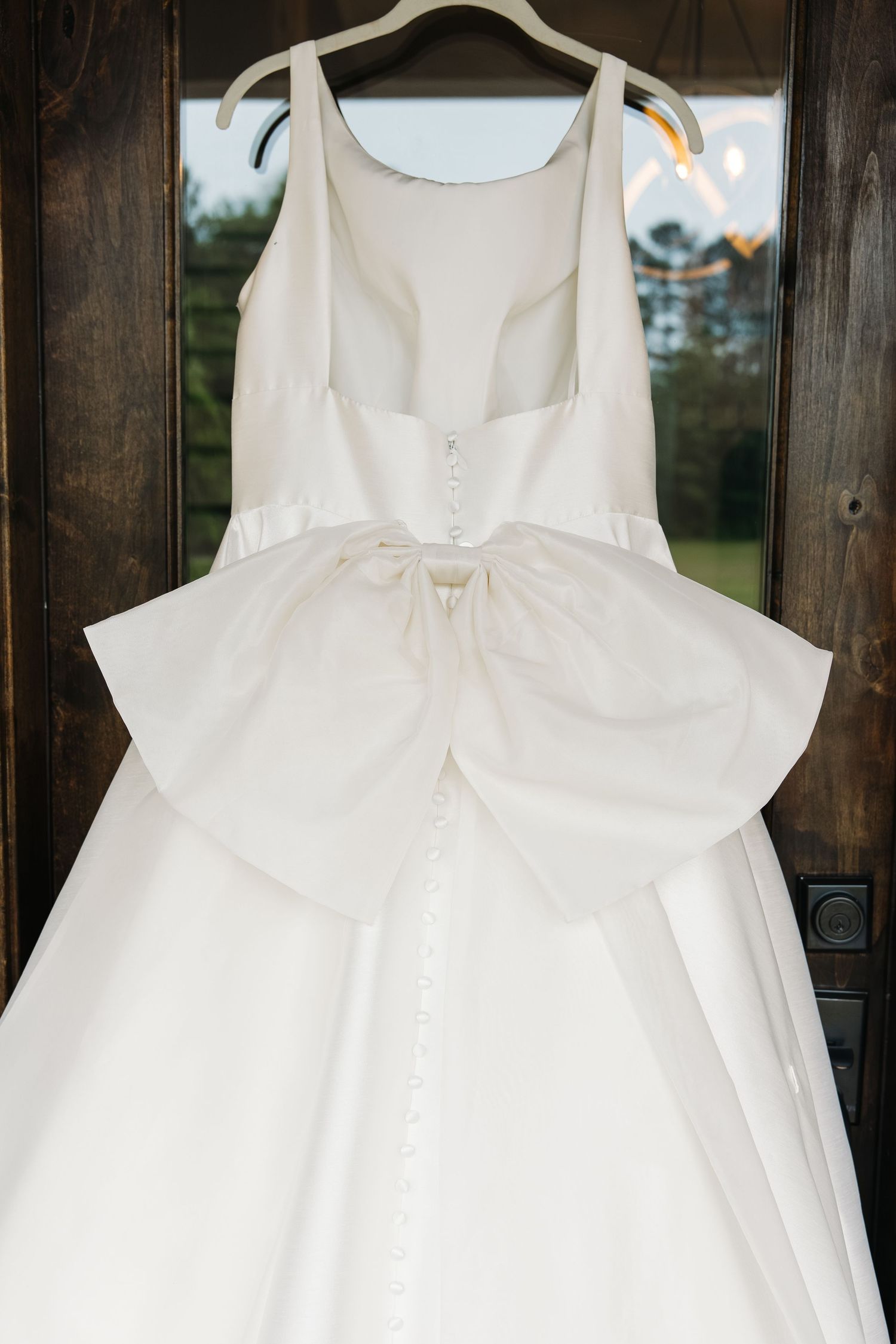 Close-up of a white satin wedding dress bodice featuring a large bow and delicate button back detail.