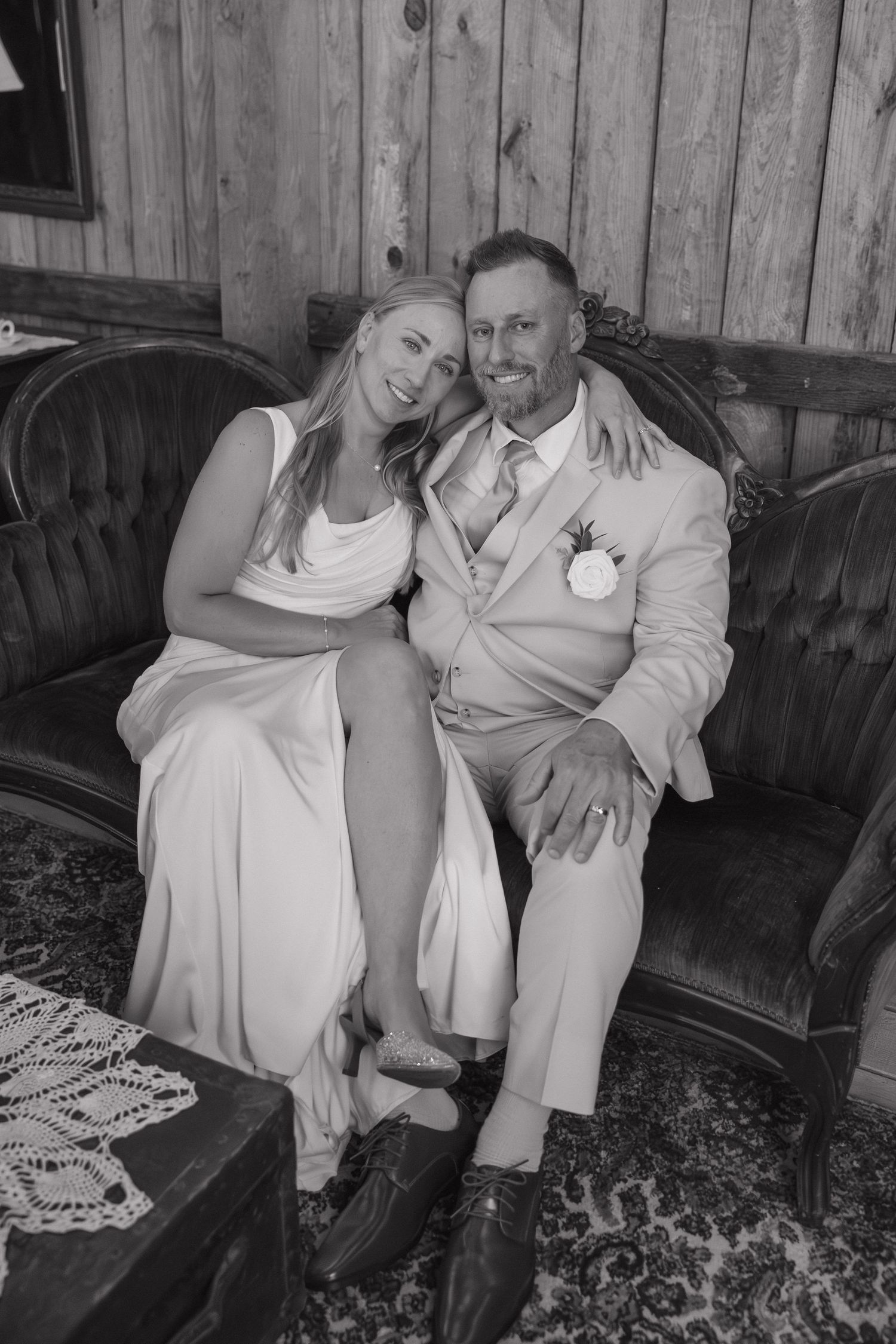 Bride and groom sitting together on a vintage sofa in a rustic barn, black and white photo.