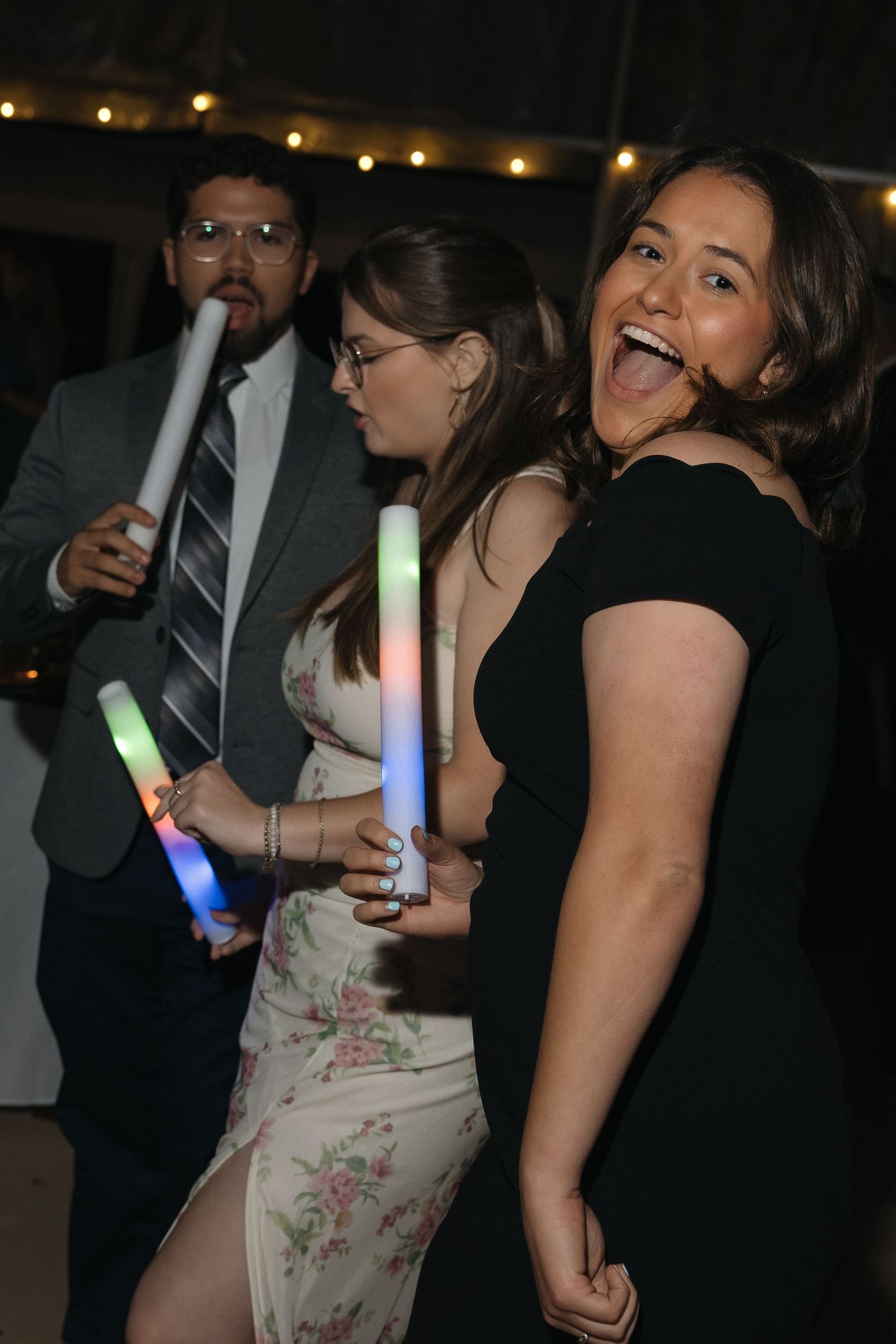 Excited wedding guests dancing with colorful LED glow sticks at lively outdoor reception party.