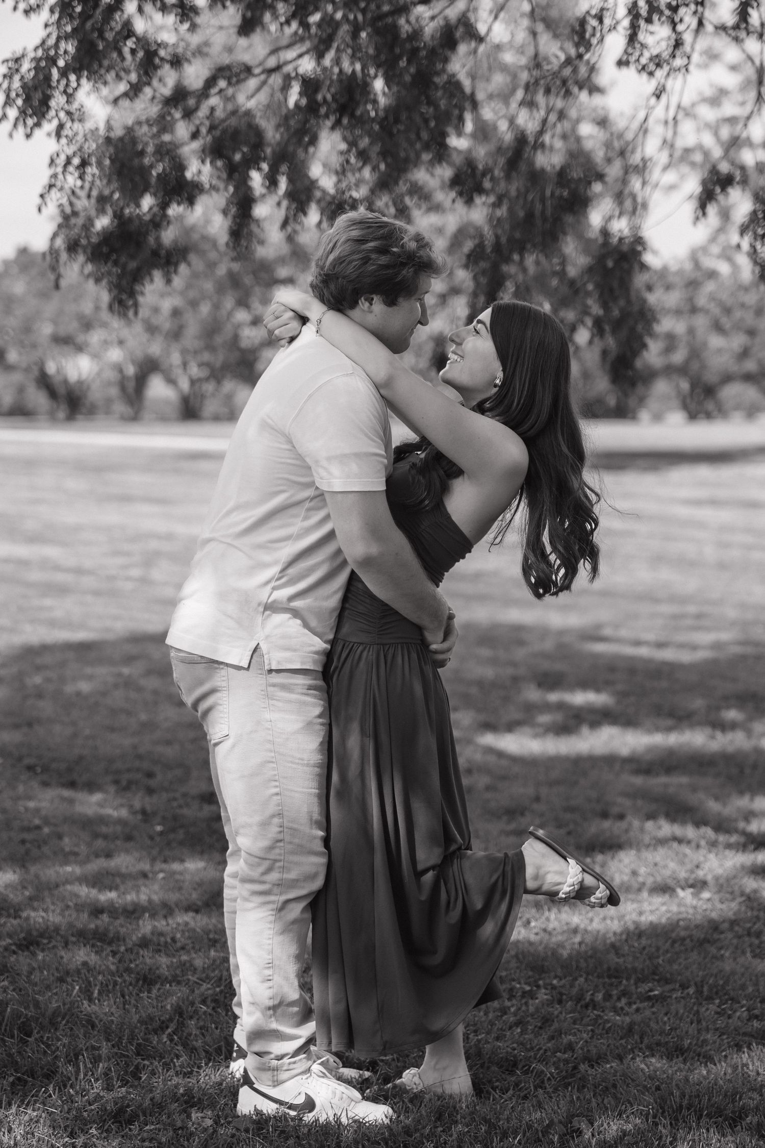 Black and white photo of a couple embracing and almost kissing in a park.