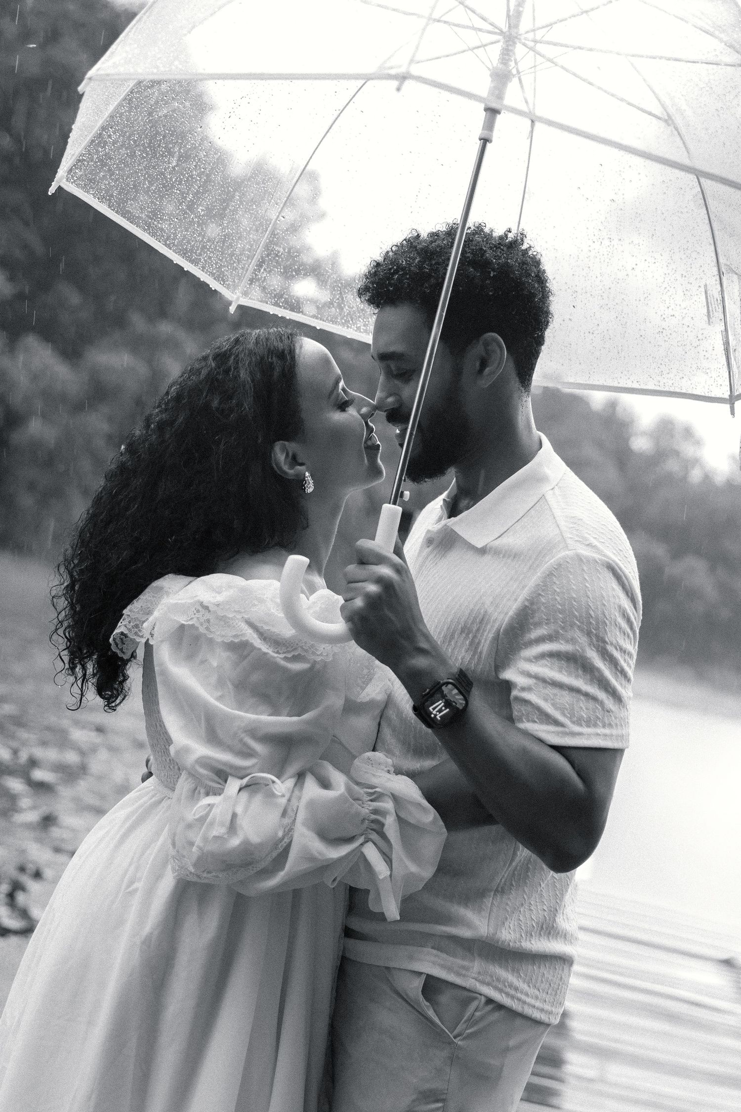 Black and white photo of a romantic couple sharing a kiss under a clear umbrella in the rain.