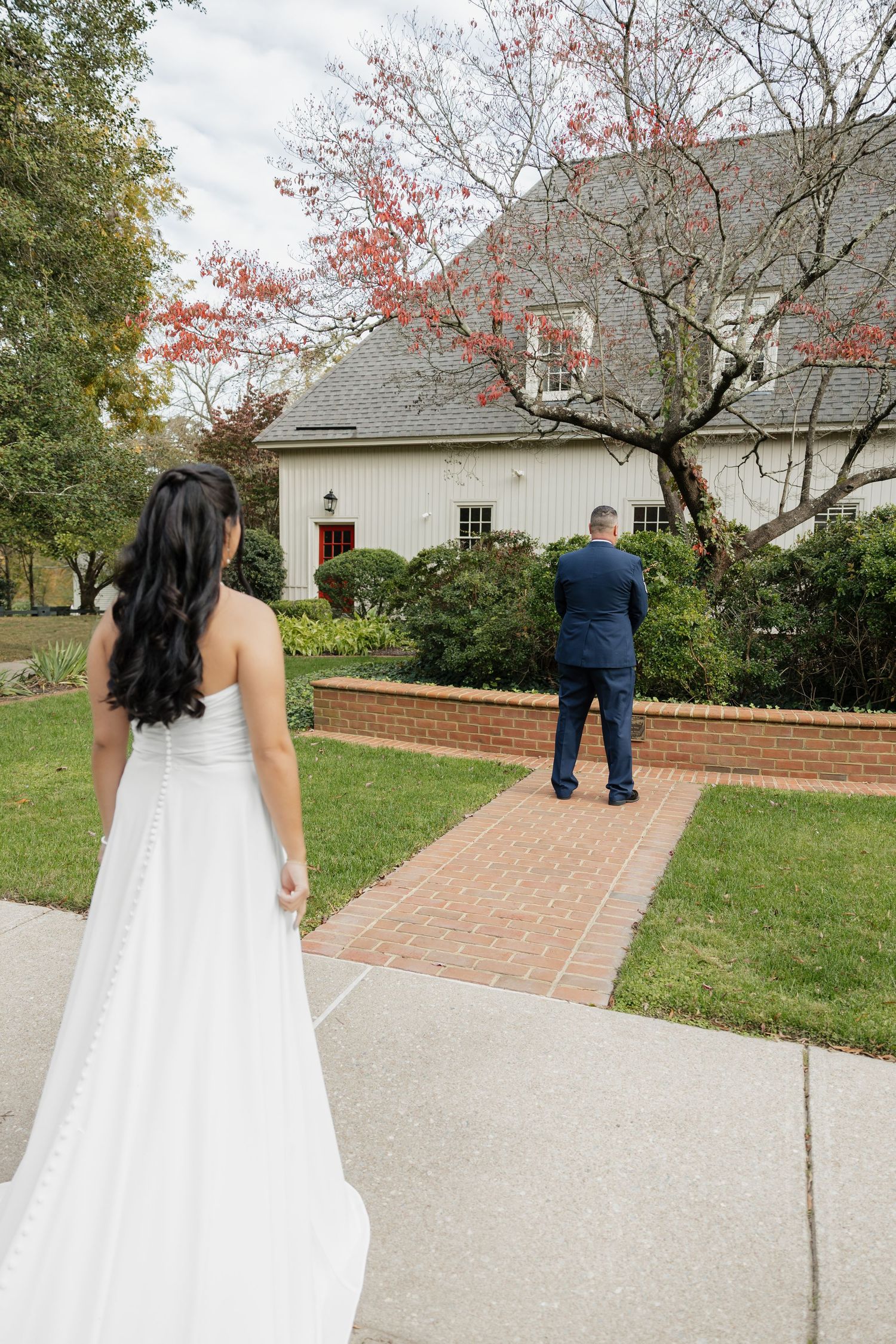 Bride in white gown approaching man in military uniform for a first look outside a white building.