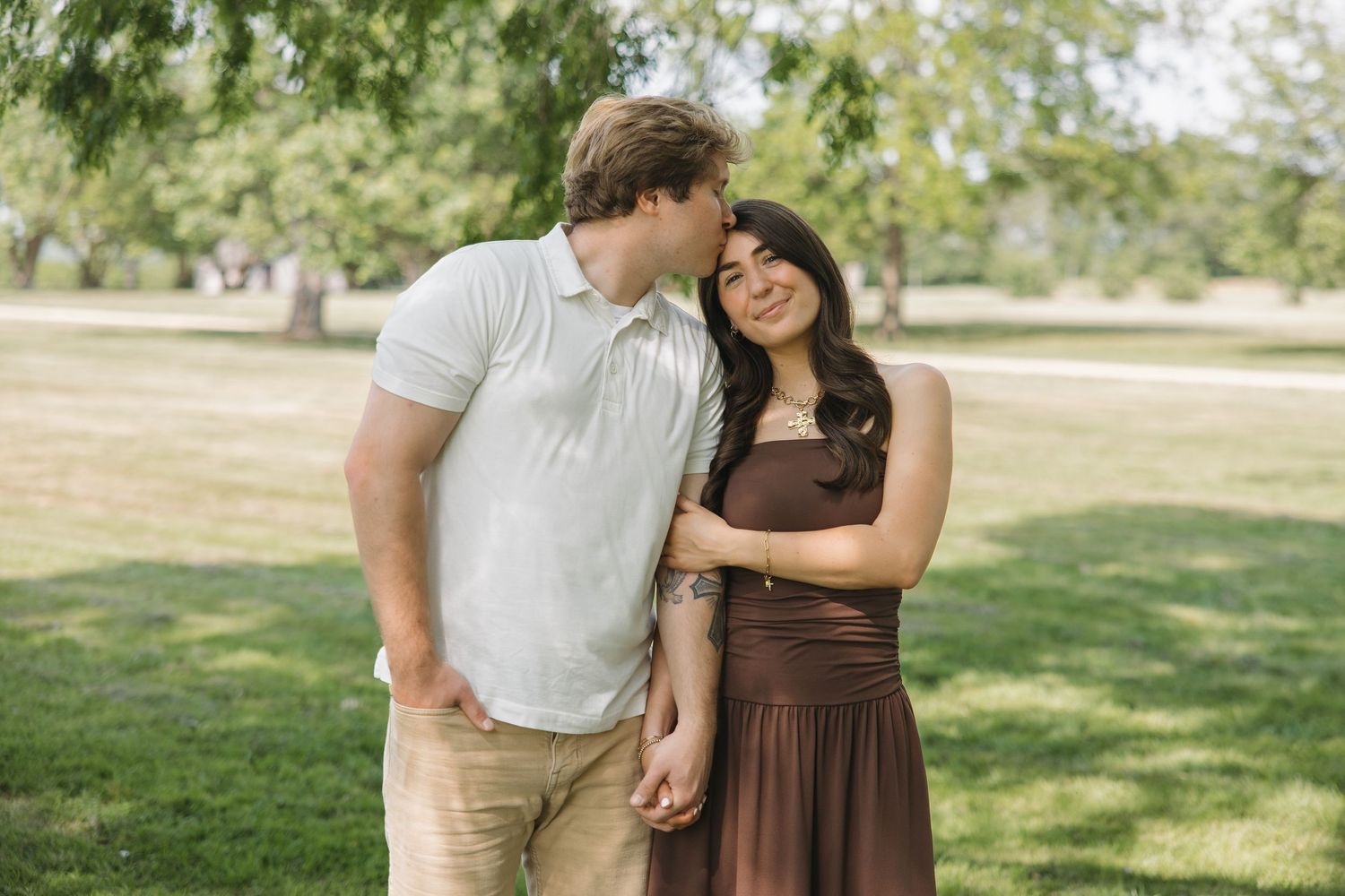 Couple standing close together smiling and holding hands in a sunny green park.