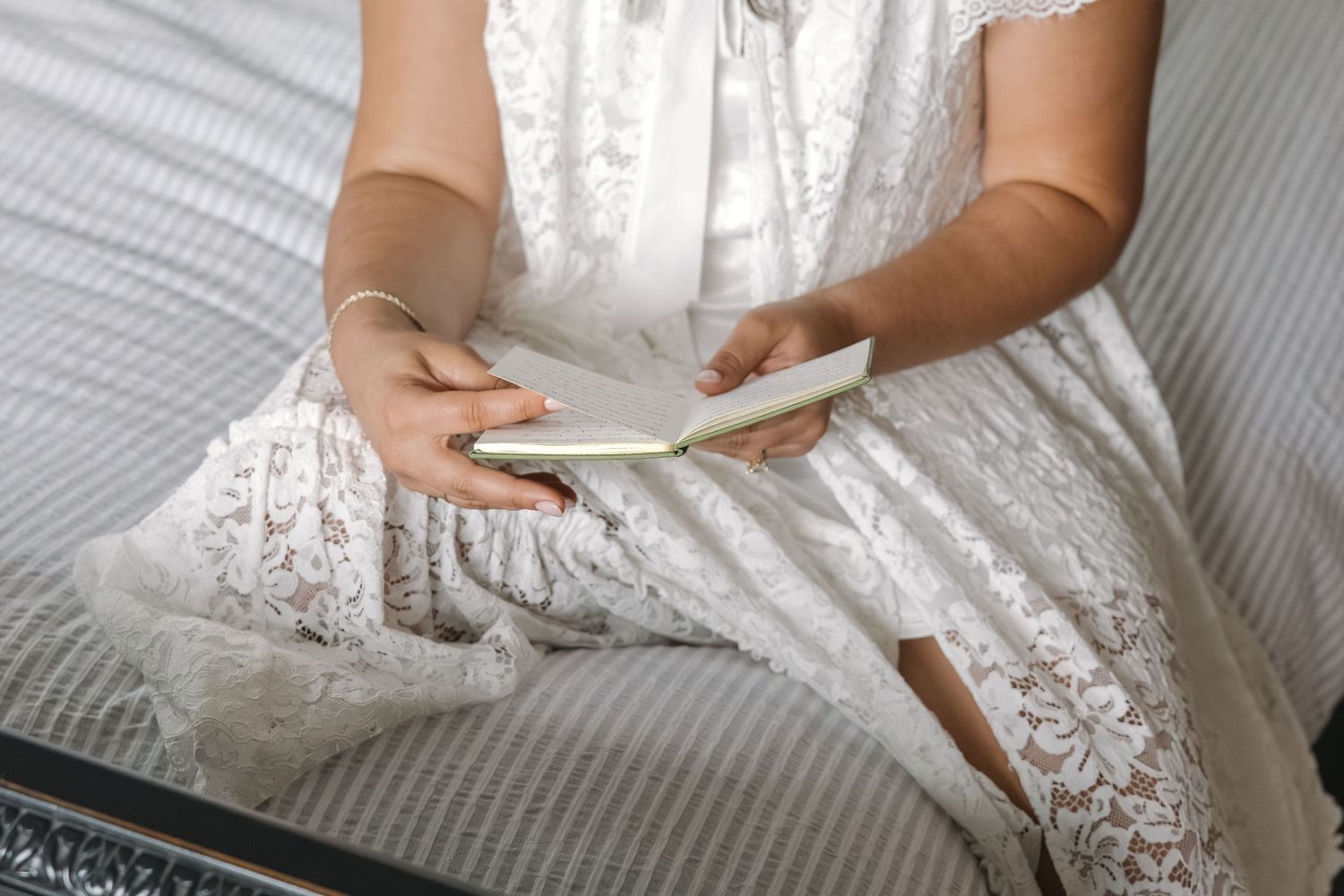 Close-up of bride in white lace wedding dress holding an open card on her lap.