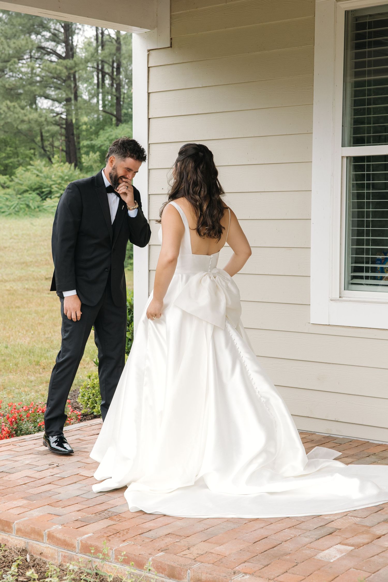 Groom emotionally kisses brides hand during romantic first look on brick porch at wedding.