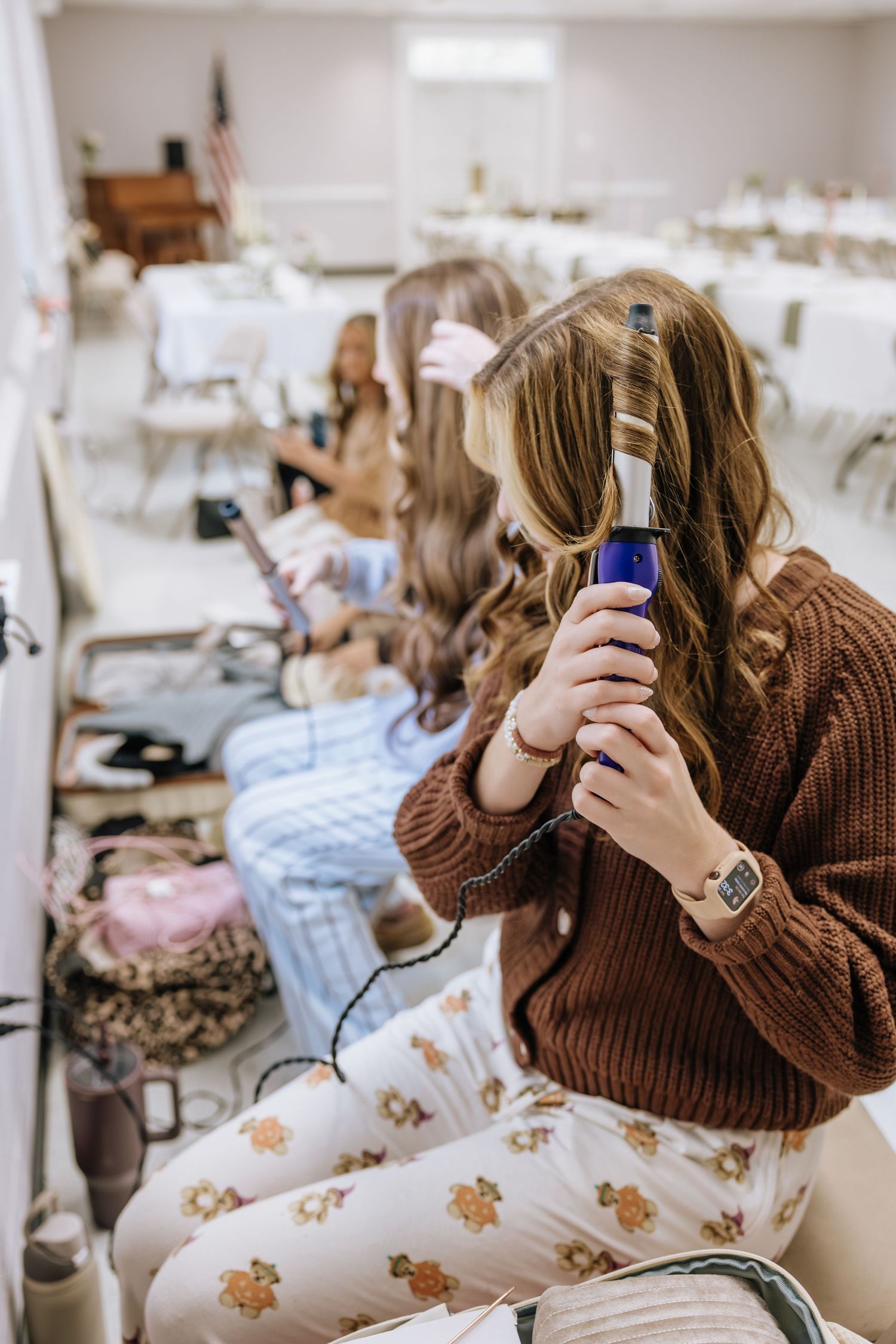 Bridesmaids in floral pajamas curl their hair while getting ready for a wedding.