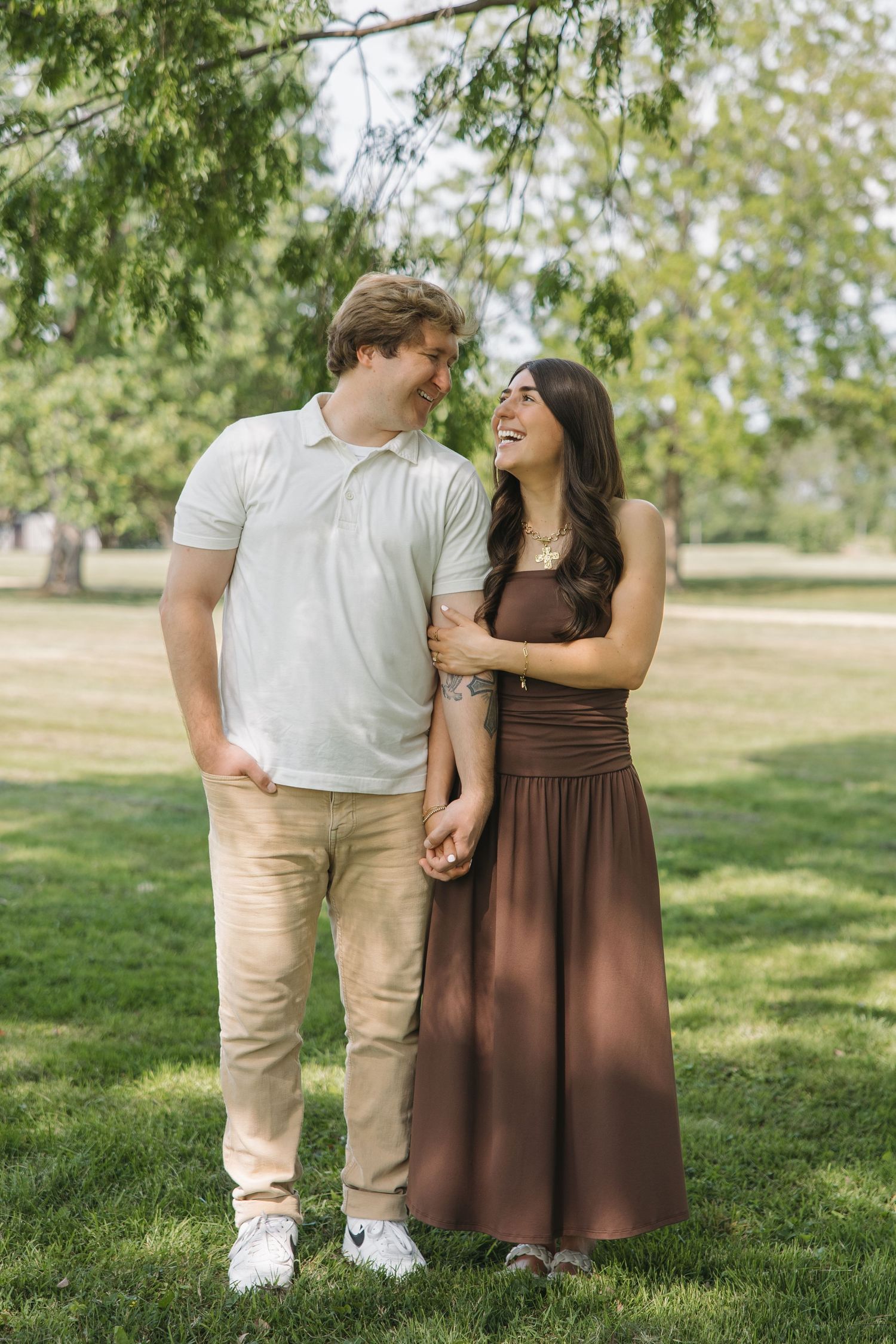 Happy couple holding hands and smiling at each other under a tree in a park.
