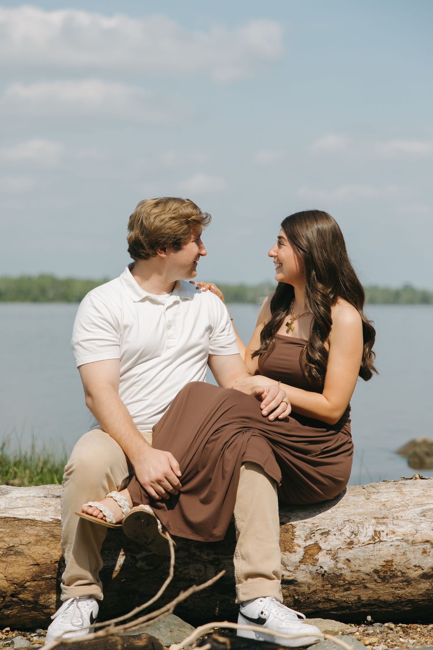 Laughing couple sitting on a driftwood log with a beautiful lake backdrop.