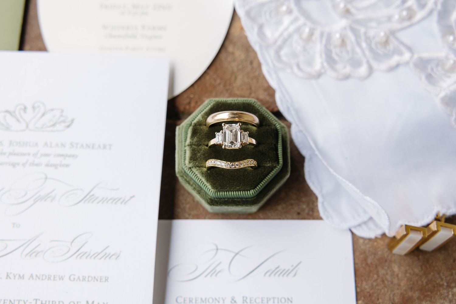 Wedding rings displayed in green velvet octagonal ring box atop elegant white wedding invitation suite.