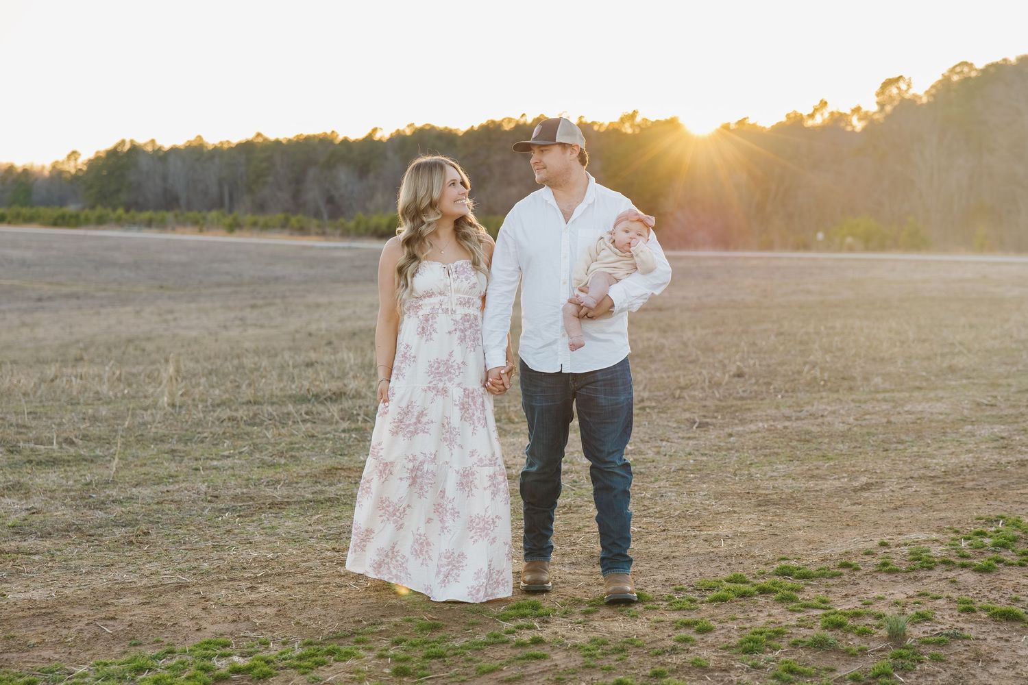 Young family walking hand in hand in an open field during a beautiful golden sunset.